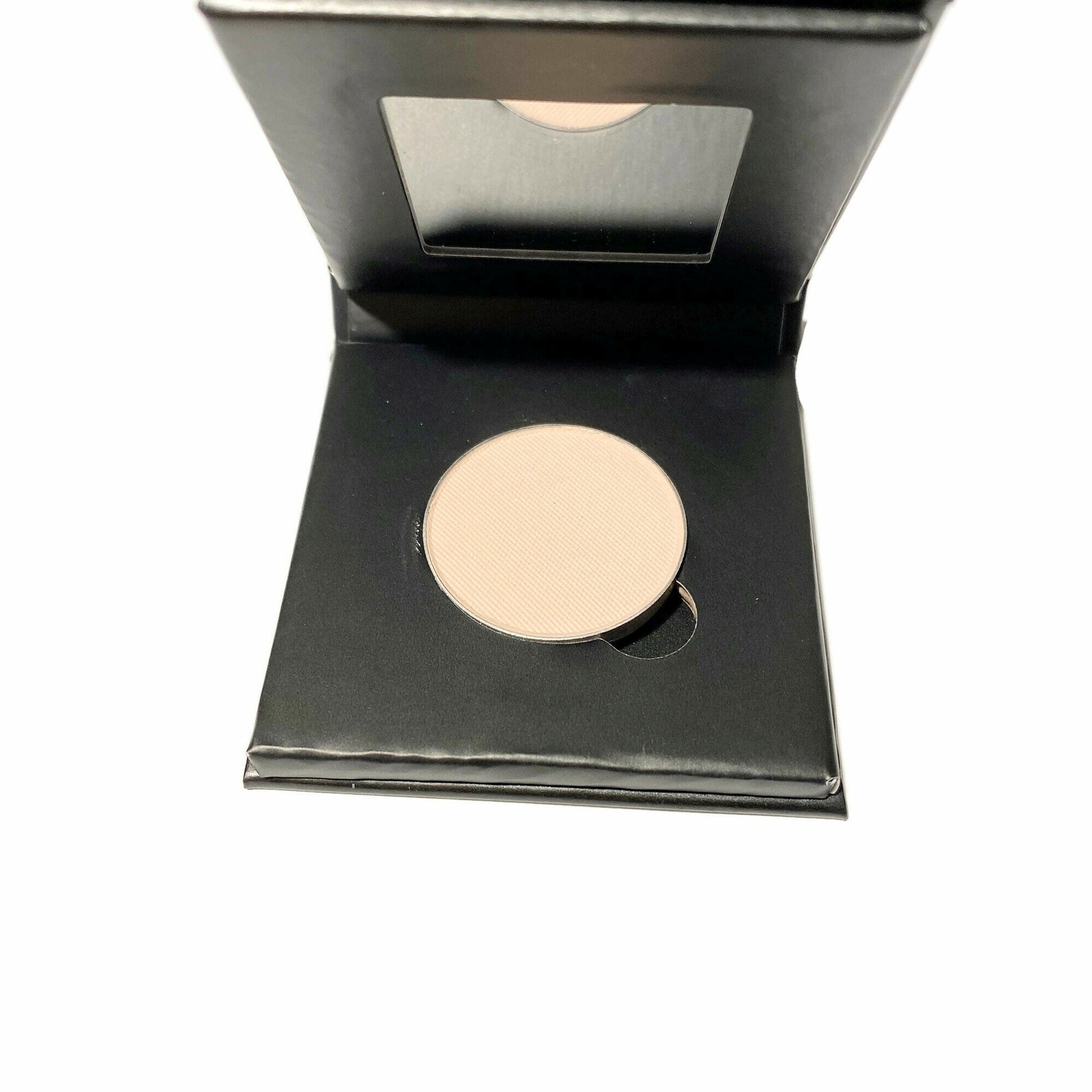 Hand applying barely bisque eyeshadow with fingertip to eyelid, showcasing soft matte finish in refillable paperboard compact