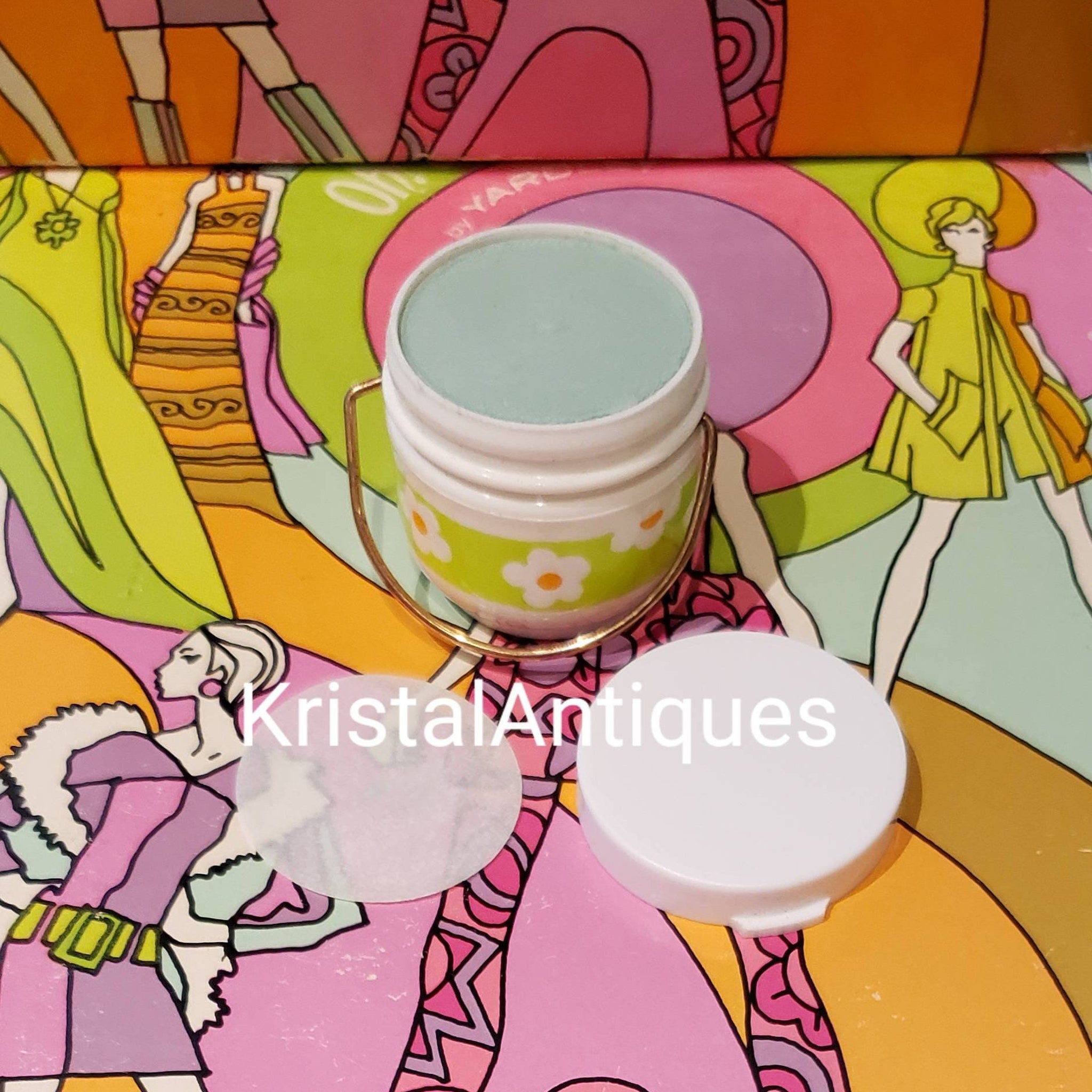 Vintage cosmetic jar with white, floral pattern, mint green powder, and gold handle detail