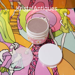Makeup compact with pink and white floral design, gold handle, and white lid on colorful background
