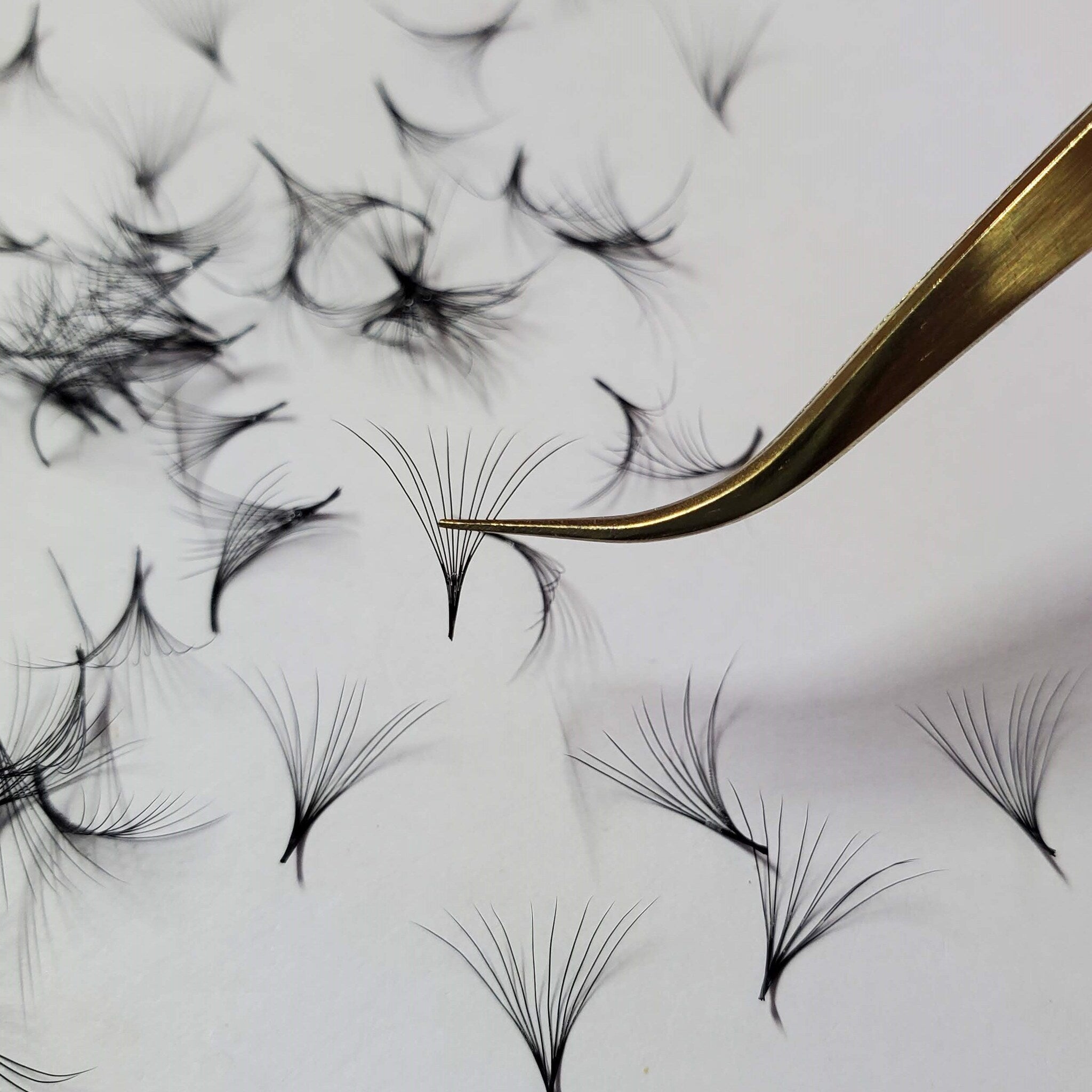 Eyelash extensions with black synthetic fibers and gold tweezers on white background