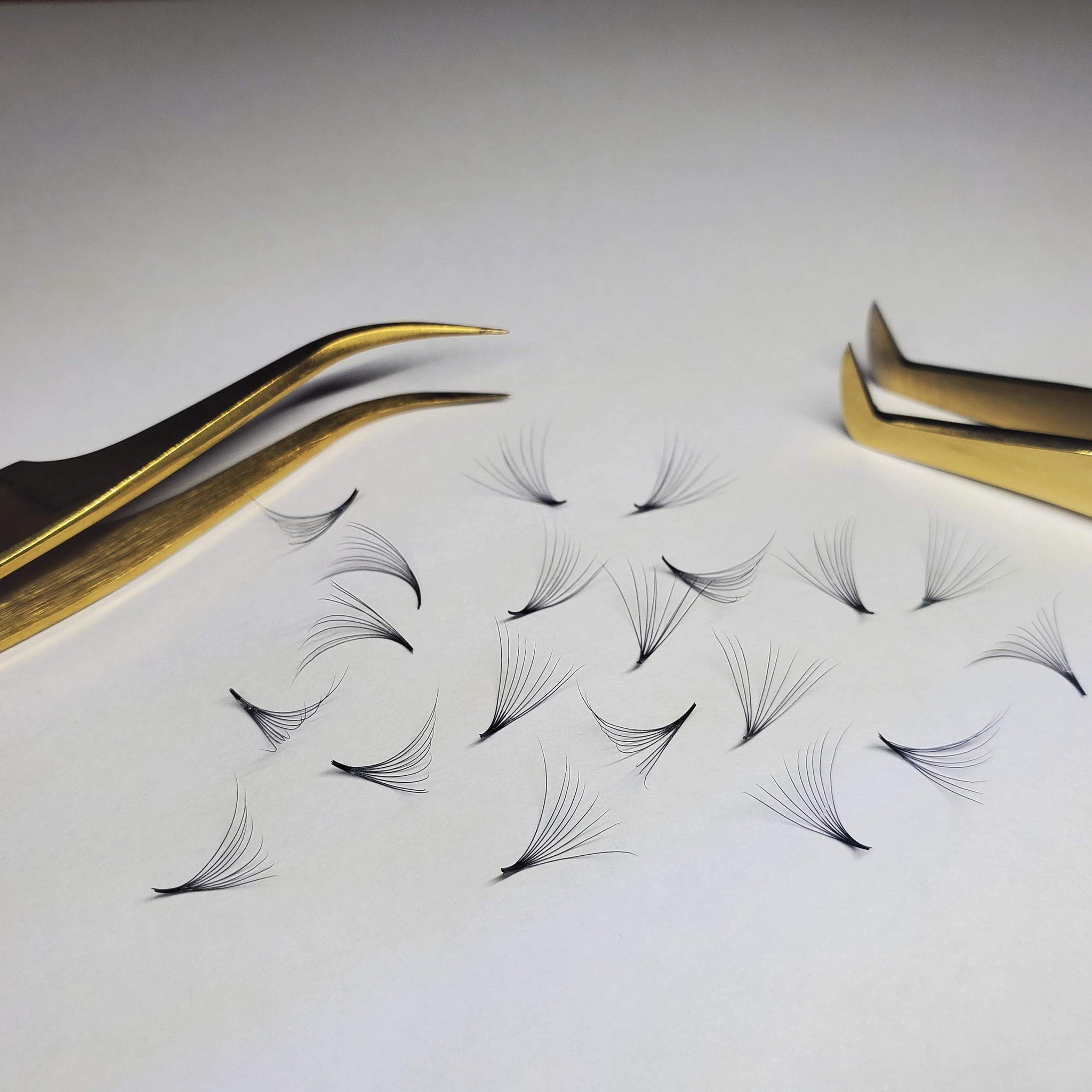 Eyelash extensions with black strands and gold tweezers on white surface