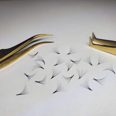 Eyelash extensions with black strands and gold tweezers on white surface