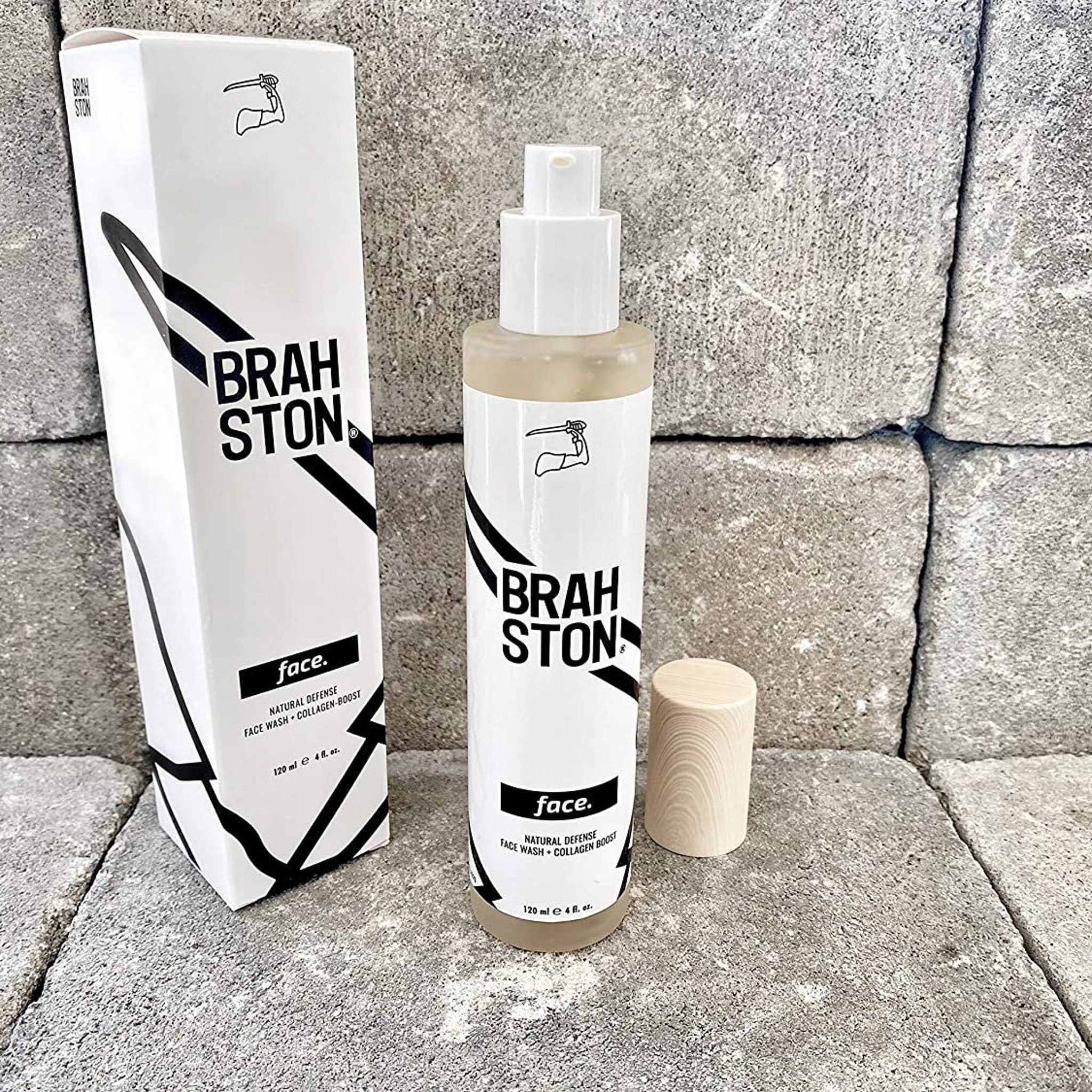 Face wash bottle with white label, black text, and wooden cap on gray stone background