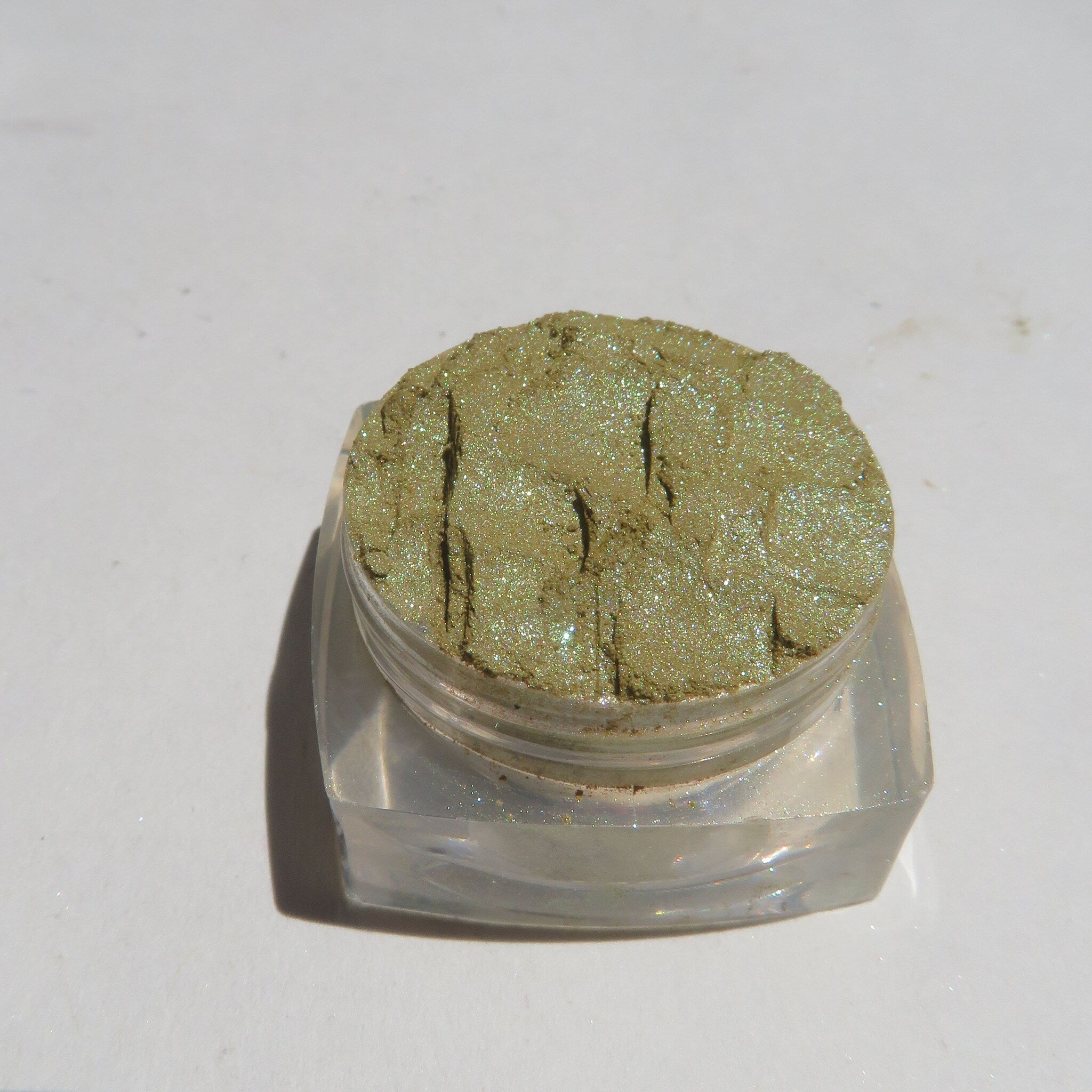 Close-up of loose shimmer eyeshadow powder showing vibrant green and gold flecks in natural light
