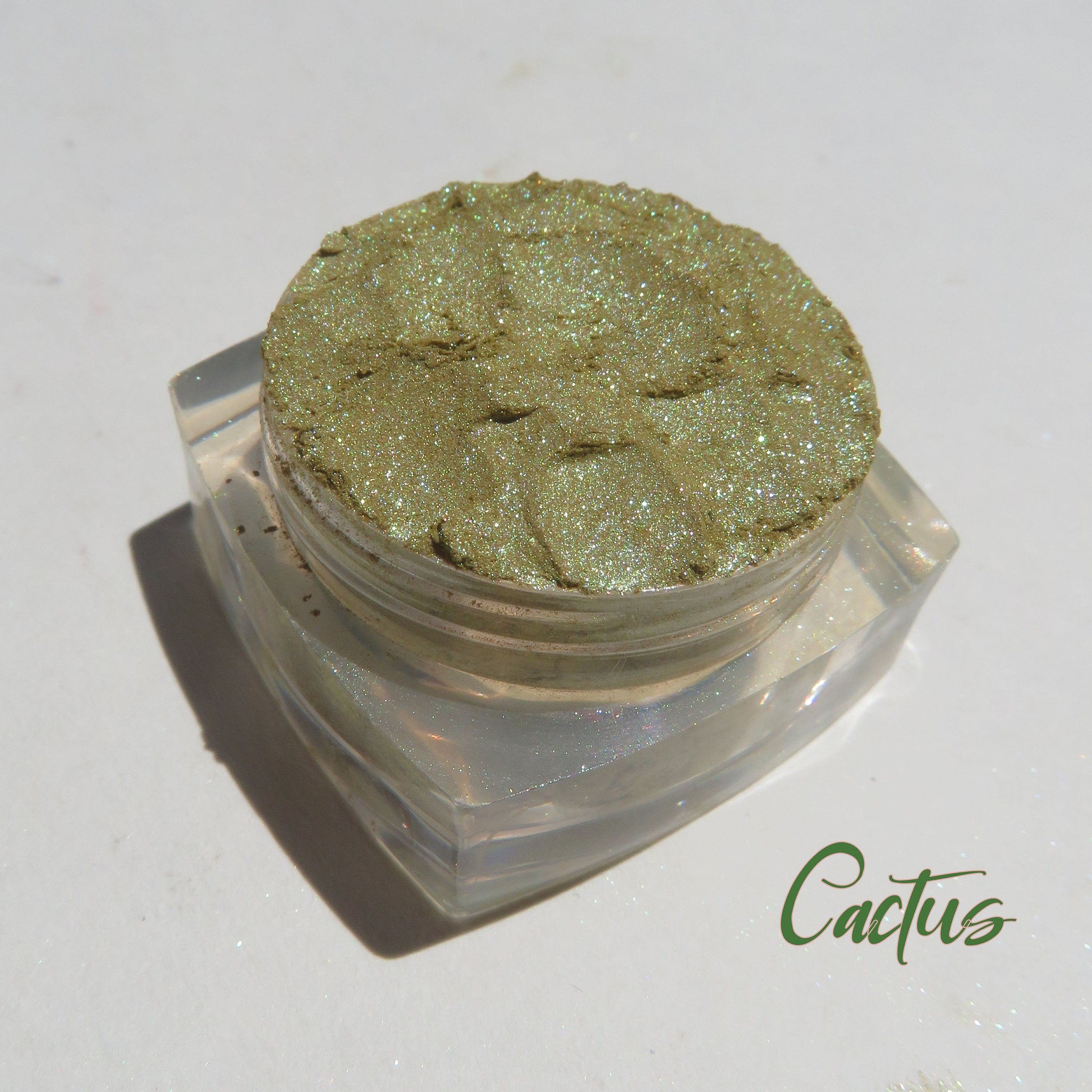 Shimmering loose mineral eyeshadow in vibrant green and gold hues, cruelty-free and vegan, displayed in a small jar.