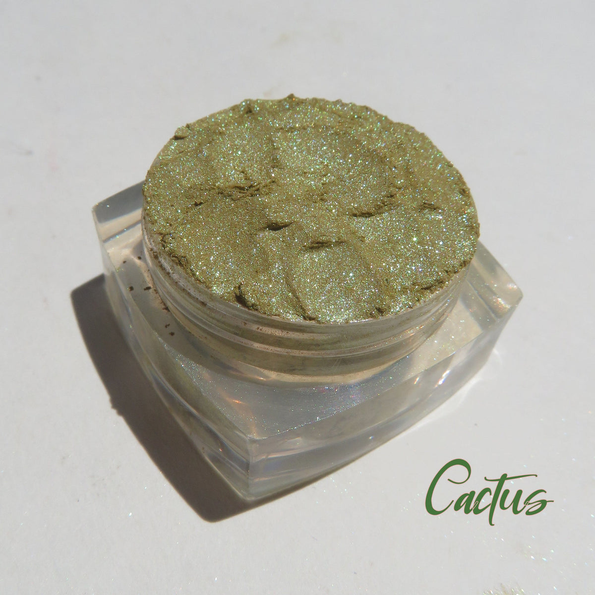 Shimmering loose mineral eyeshadow in vibrant green and gold hues, cruelty-free and vegan, displayed in a small jar.