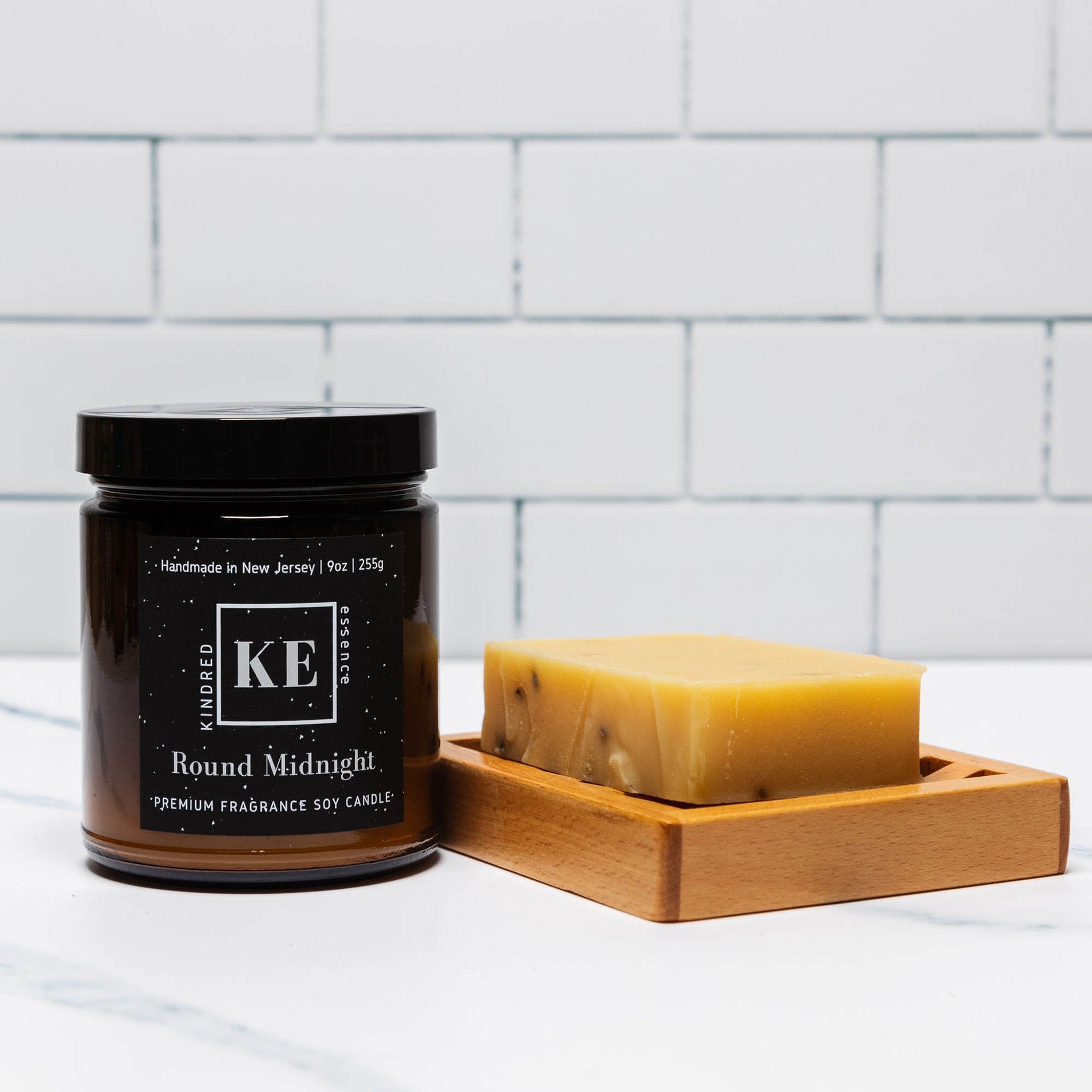 Soy candle in brown glass jar with black label and yellow soap bar on wood tray
