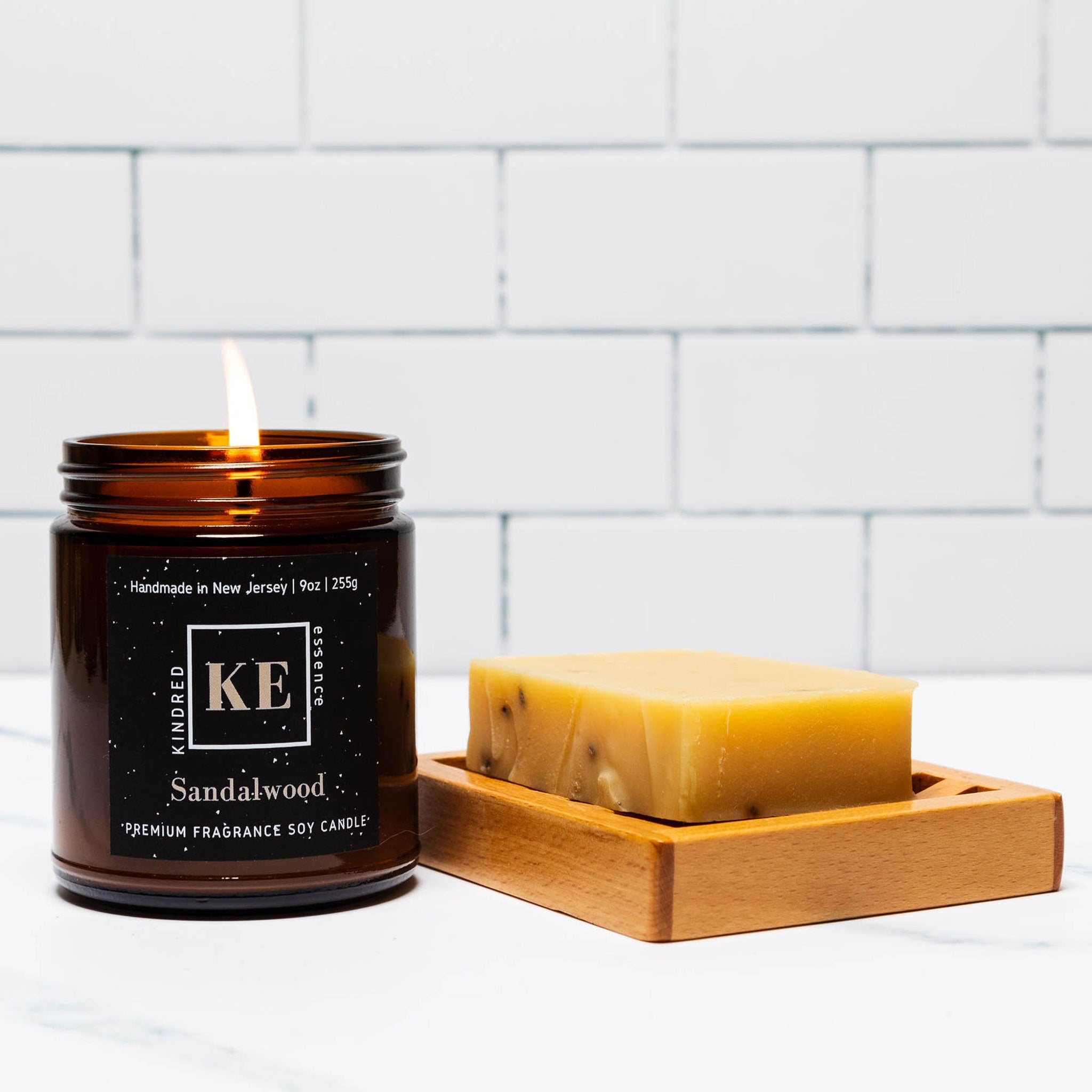Soy candle with brown glass jar, burning flame, and KE Kindred label next to soap bar