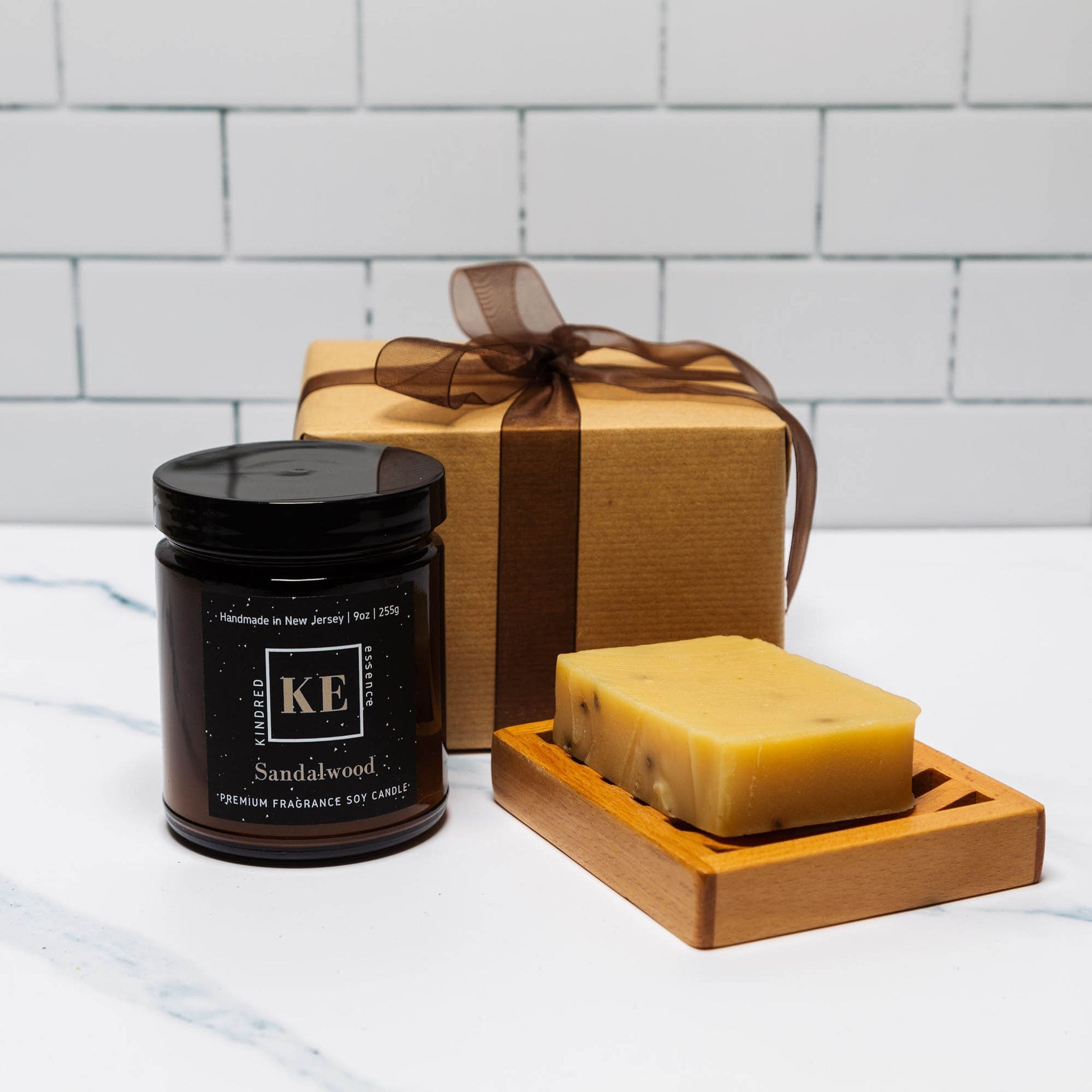 Sandalwood candle in a black jar, brown gift box with ribbon, and yellow soap on wooden tray