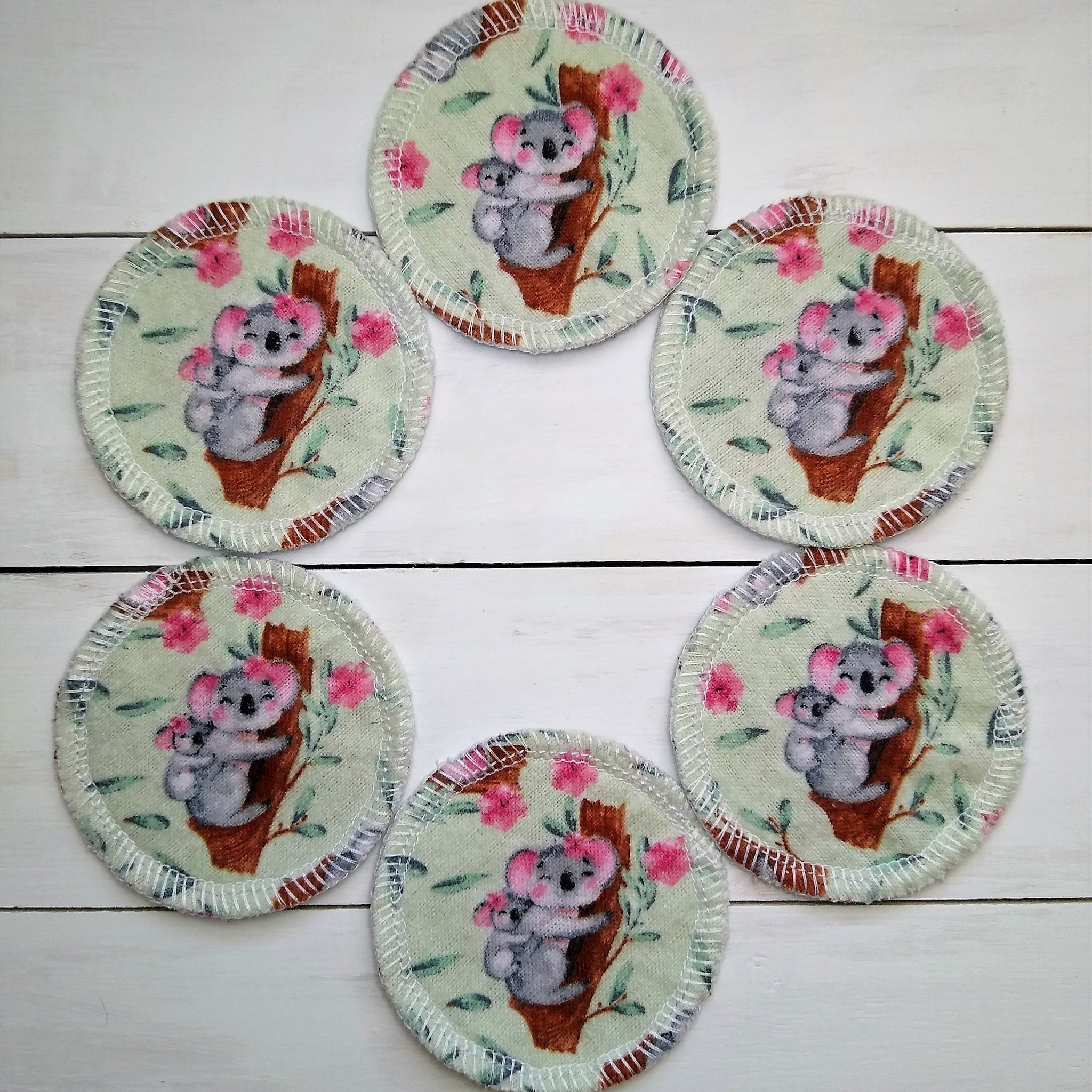 Reusable pads with koala print, light green fabric, pink flowers, and white stitching around the edge.