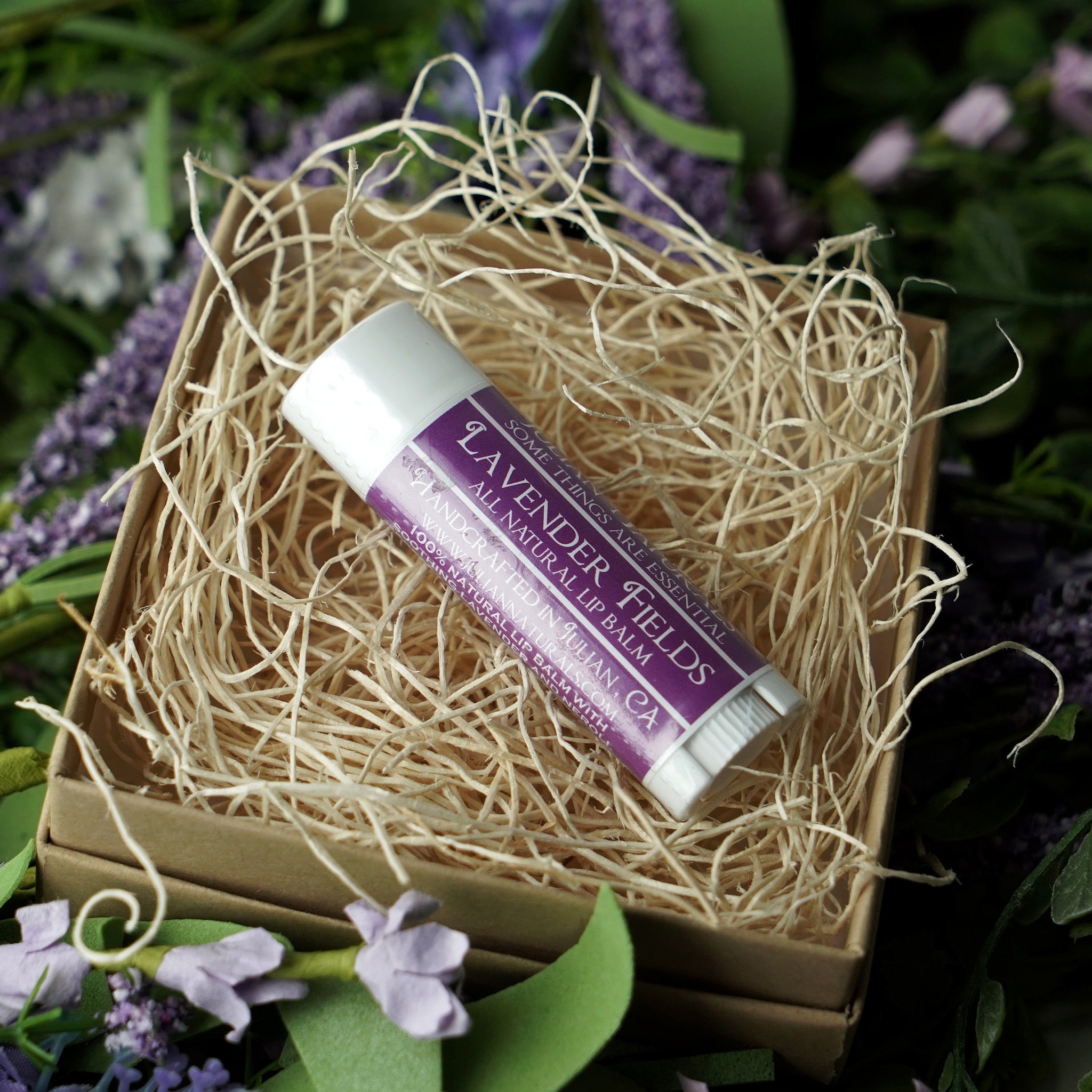Lip balm tube with white, purple label, and natural wood shavings in a box.