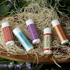 Lip balm tubes in white, red, orange, purple, and blue with text, nestled in straw