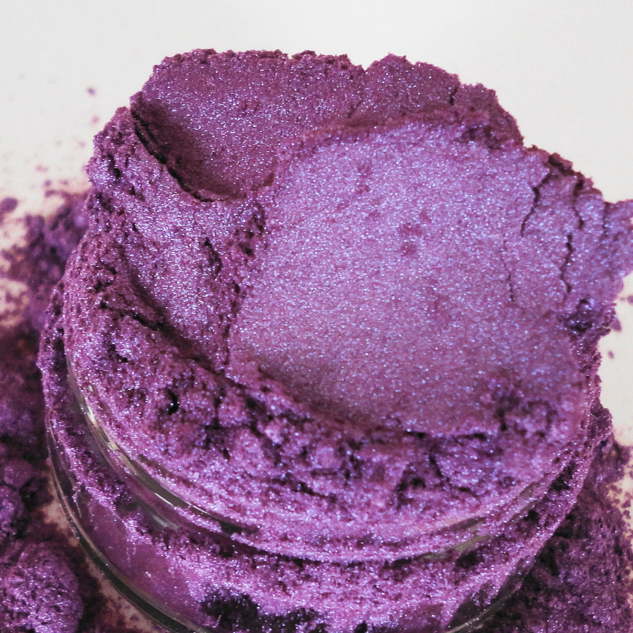 Purple eyeshadow powder with glitter, in a glass jar, showing texture and shimmer