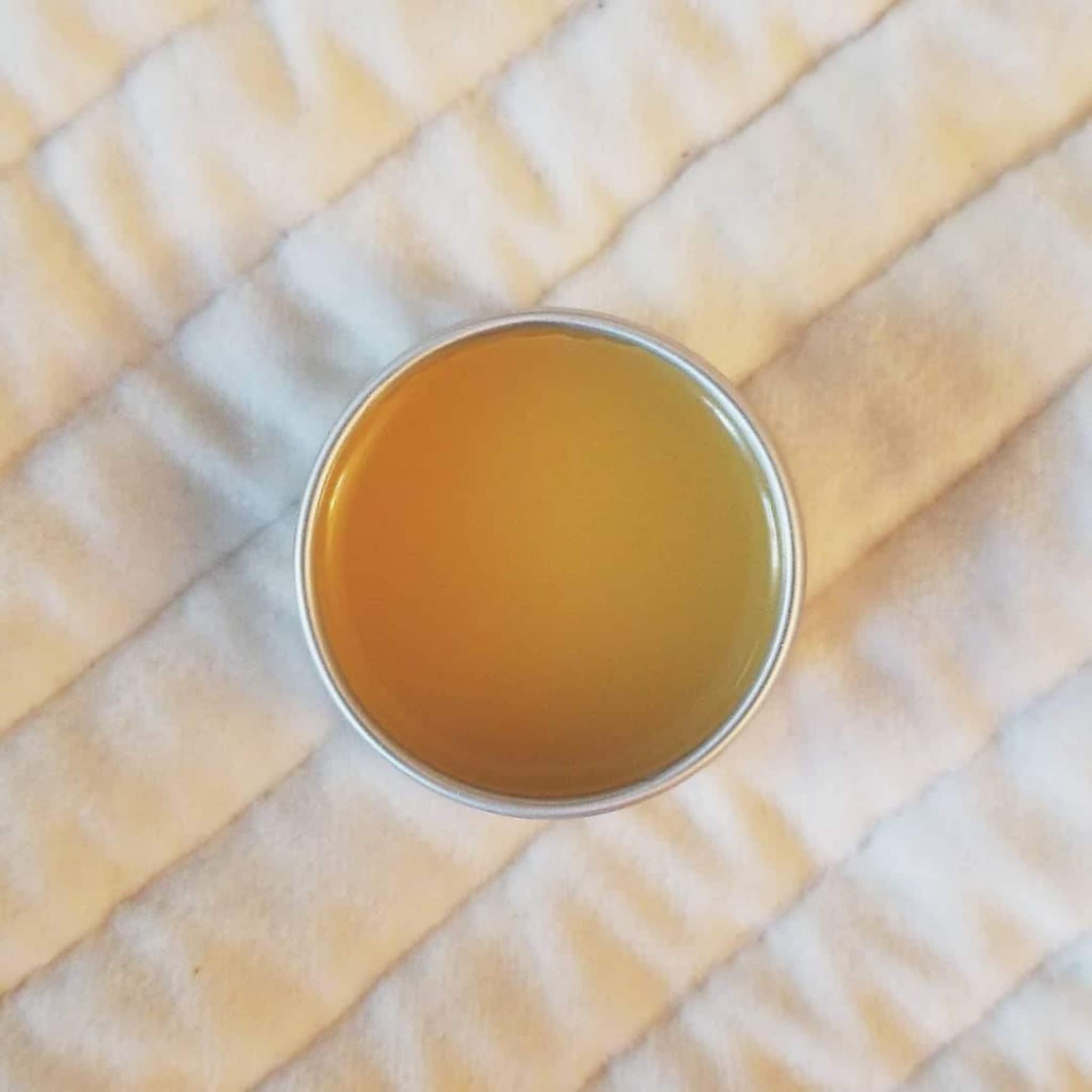 Lip balm in a silver tin with golden yellow color, sitting on white quilted fabric