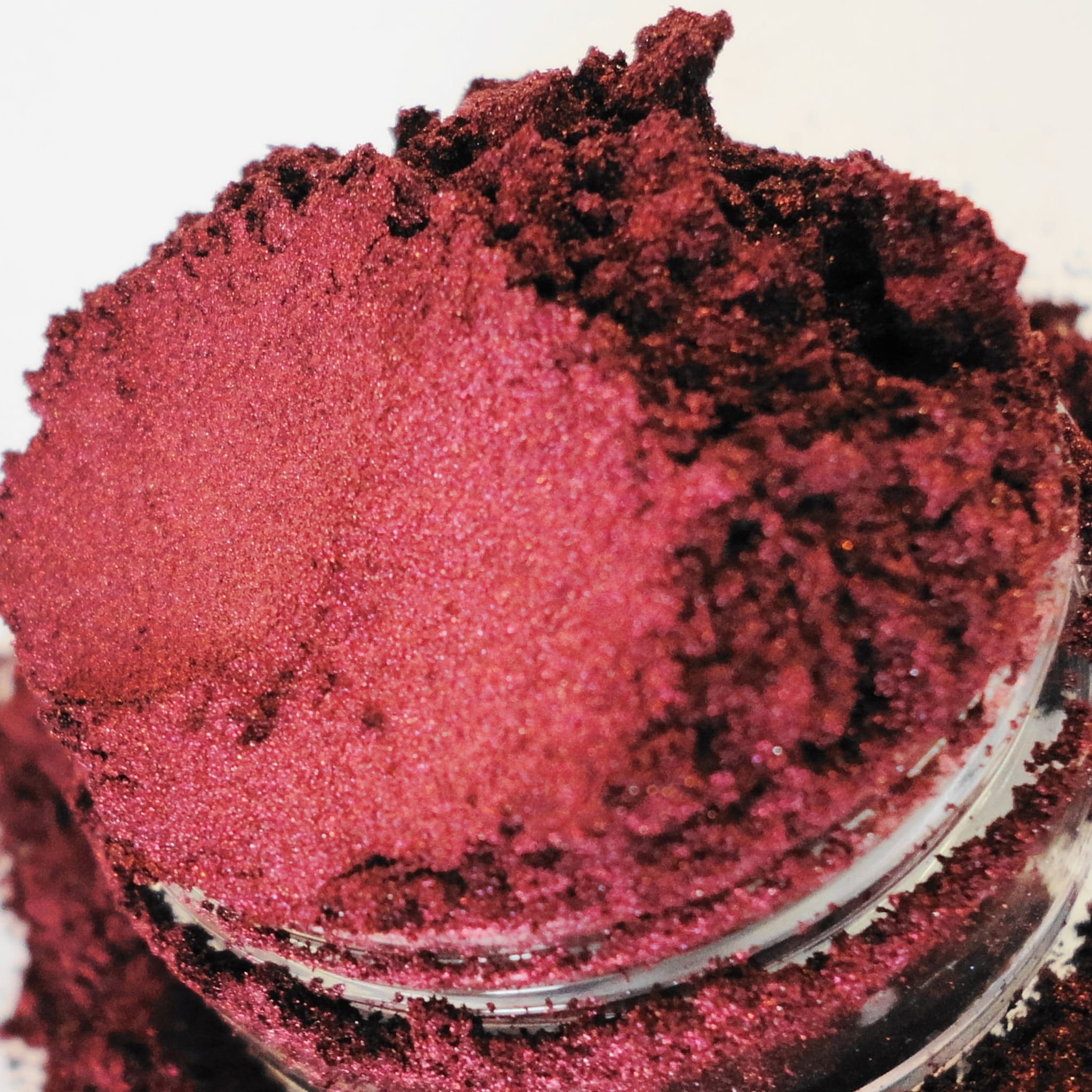 Reddish-pink powder with glitter particles in clear container, close-up view