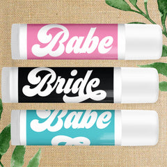 Lip balm tubes with pink, black, and teal color bands, white text, and white caps