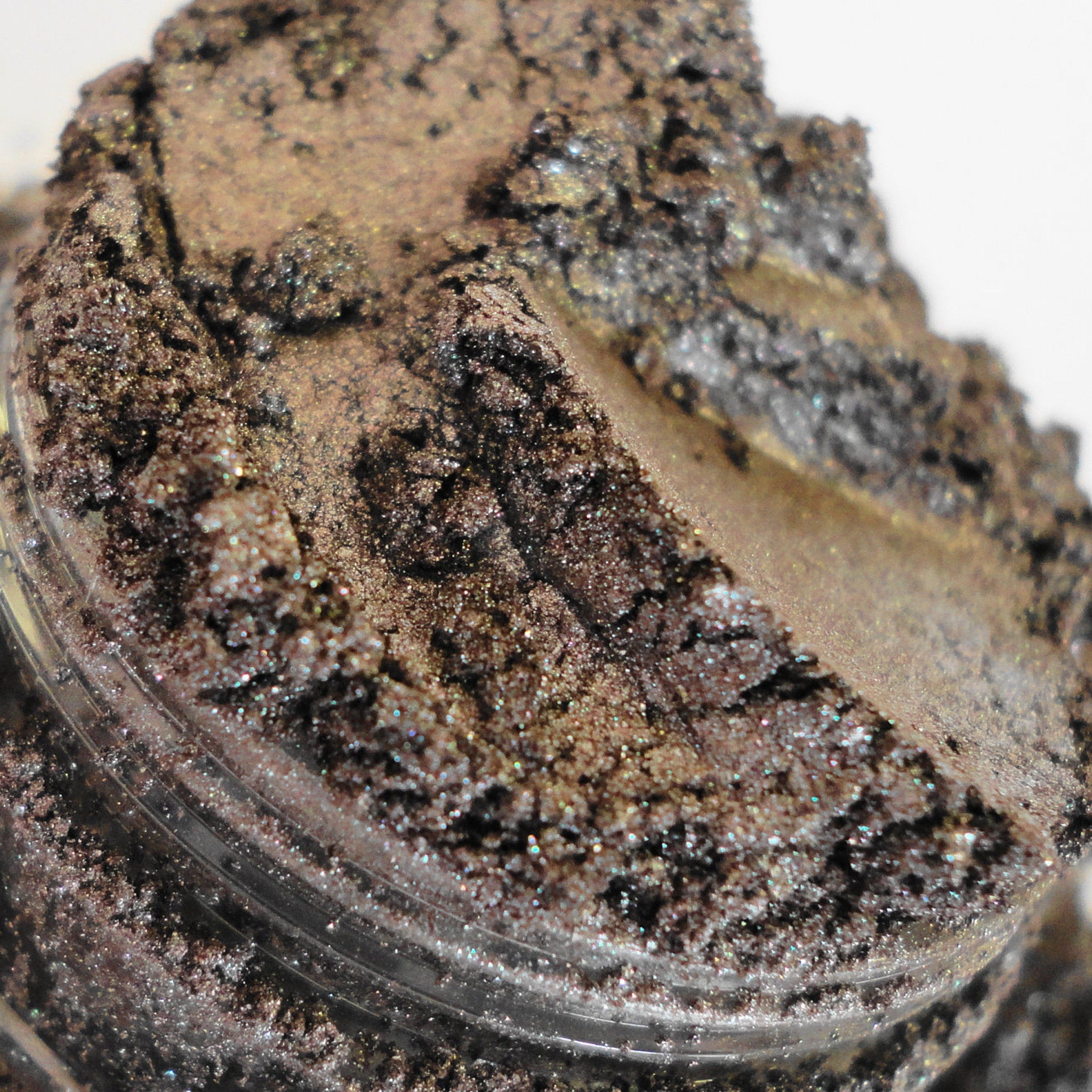 Glitter eyeshadow in brown and gold with a textured appearance, in a clear container