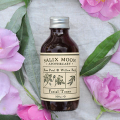 Facial Toner bottle, brown glass with silver cap, surrounded by pink flowers and green leaves, Salix Moon brand