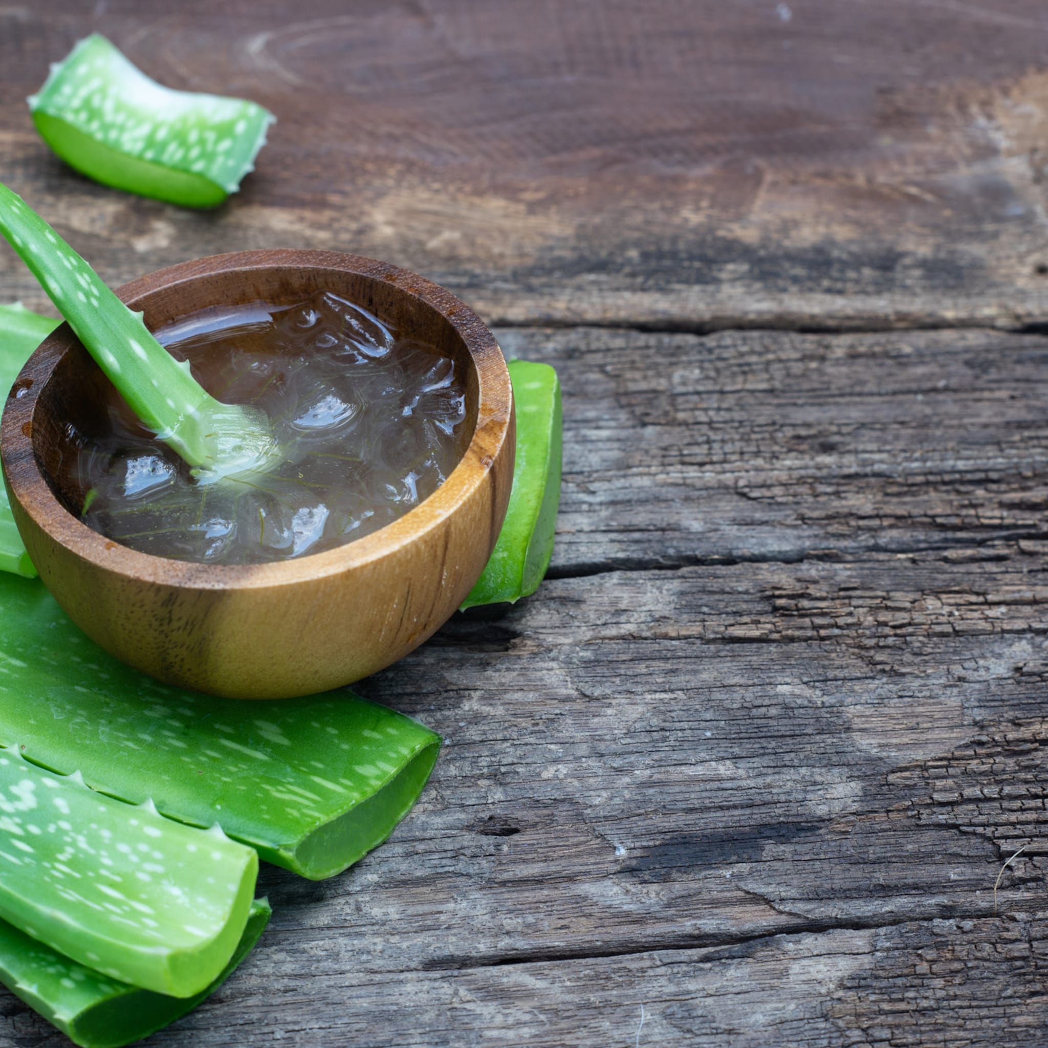 Aloe vera leaves with green color, wooden bowl with gel, and wooden background