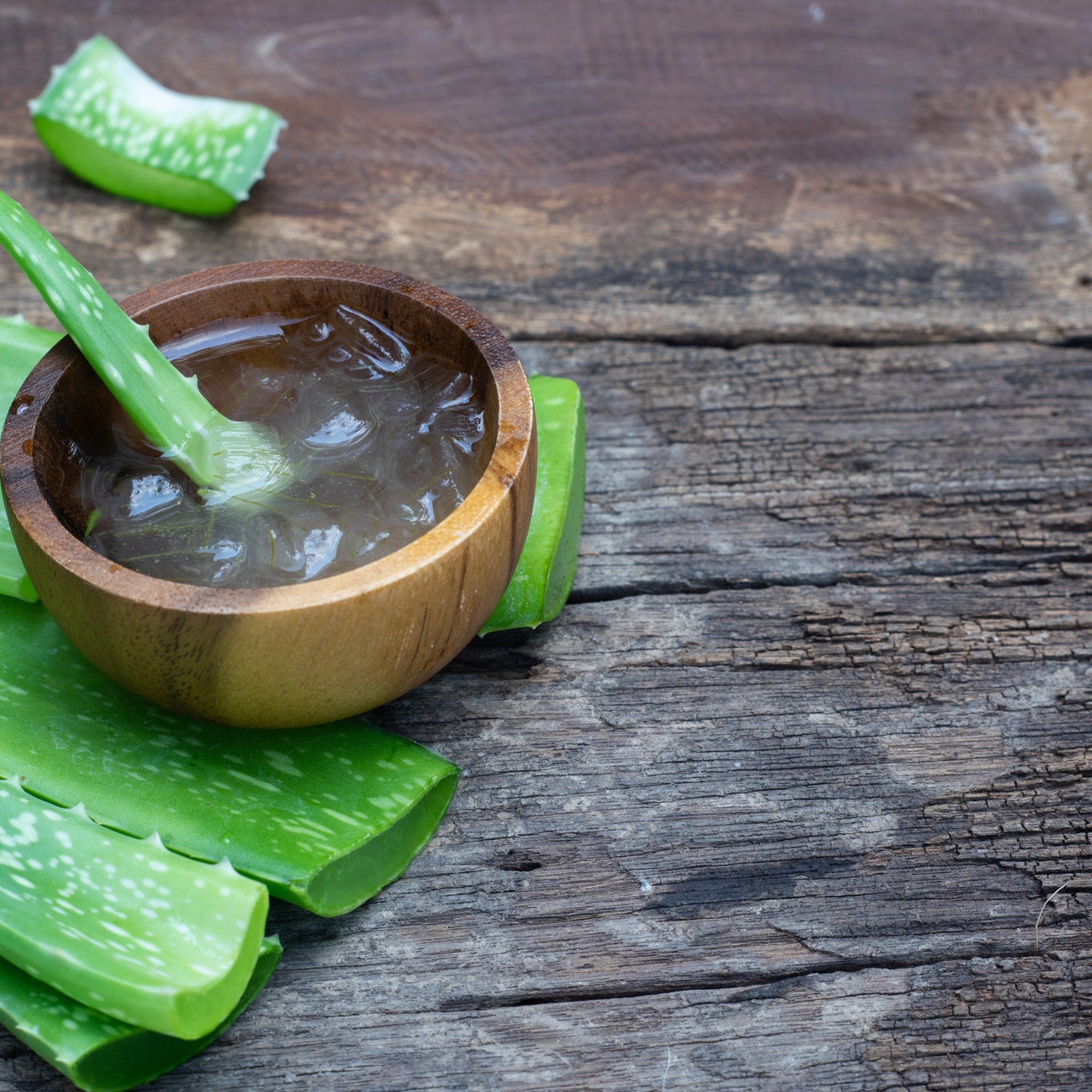 Aloe vera leaves and gel in wooden bowl on rustic wood surface, green and brown tones