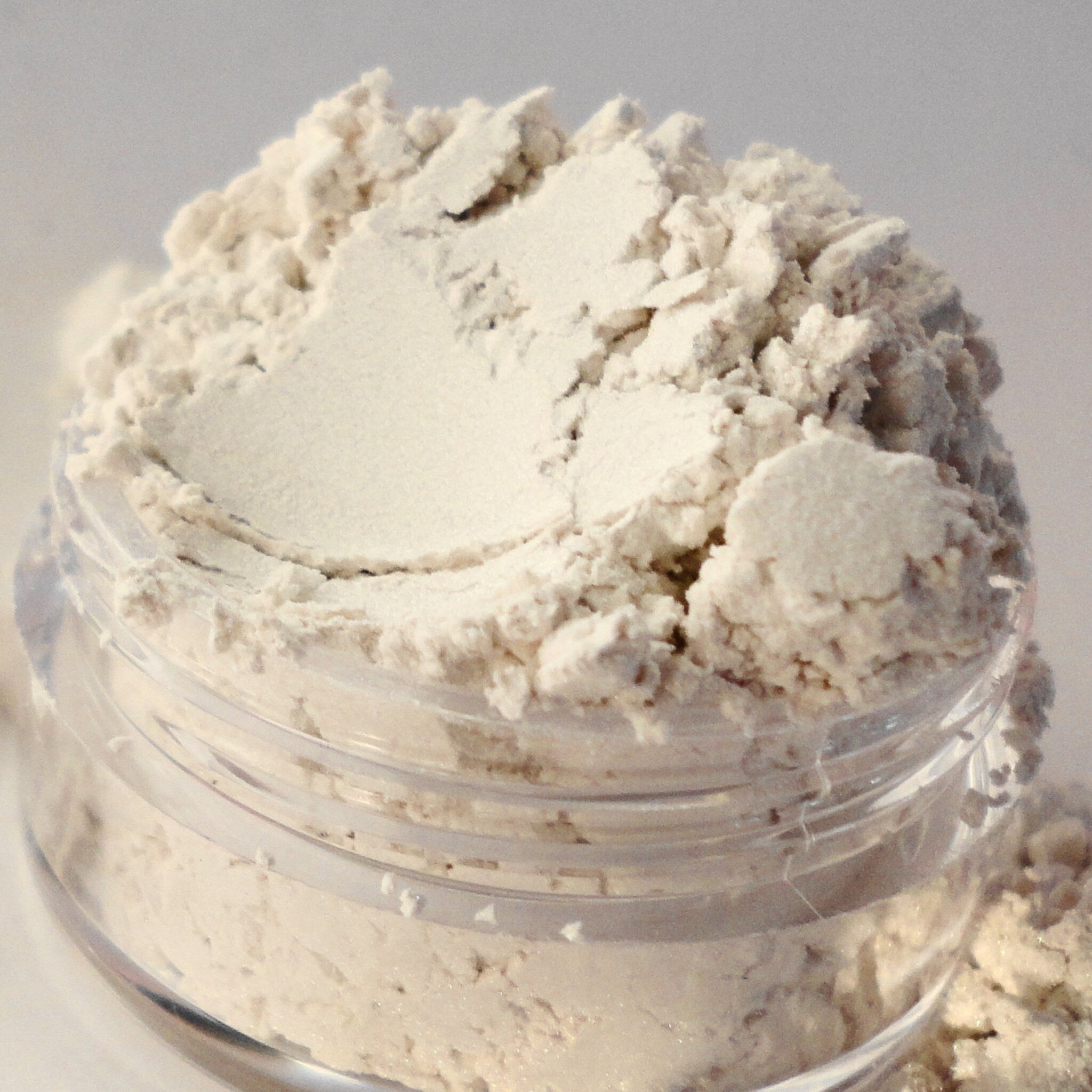 Close-up of silver shimmer eye shadow powder with glitter particles in a sifter jar, showcasing texture and sparkle