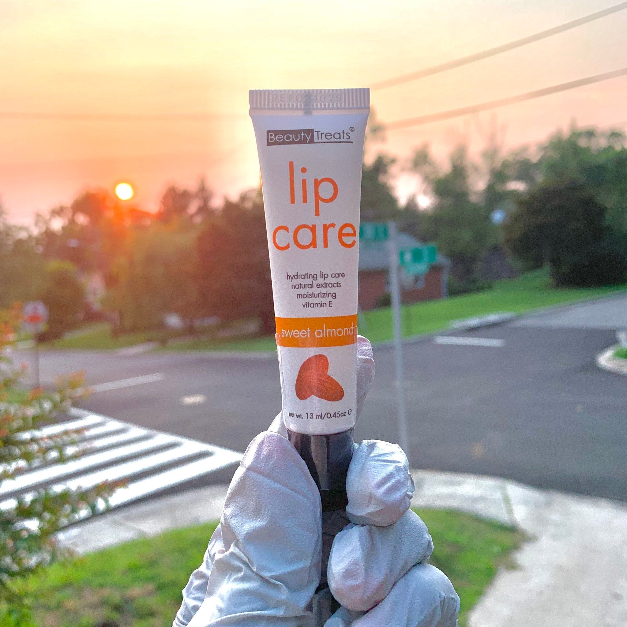 Lip care tube with white and orange text, held by gloved hands, Beauty Treats brand visible