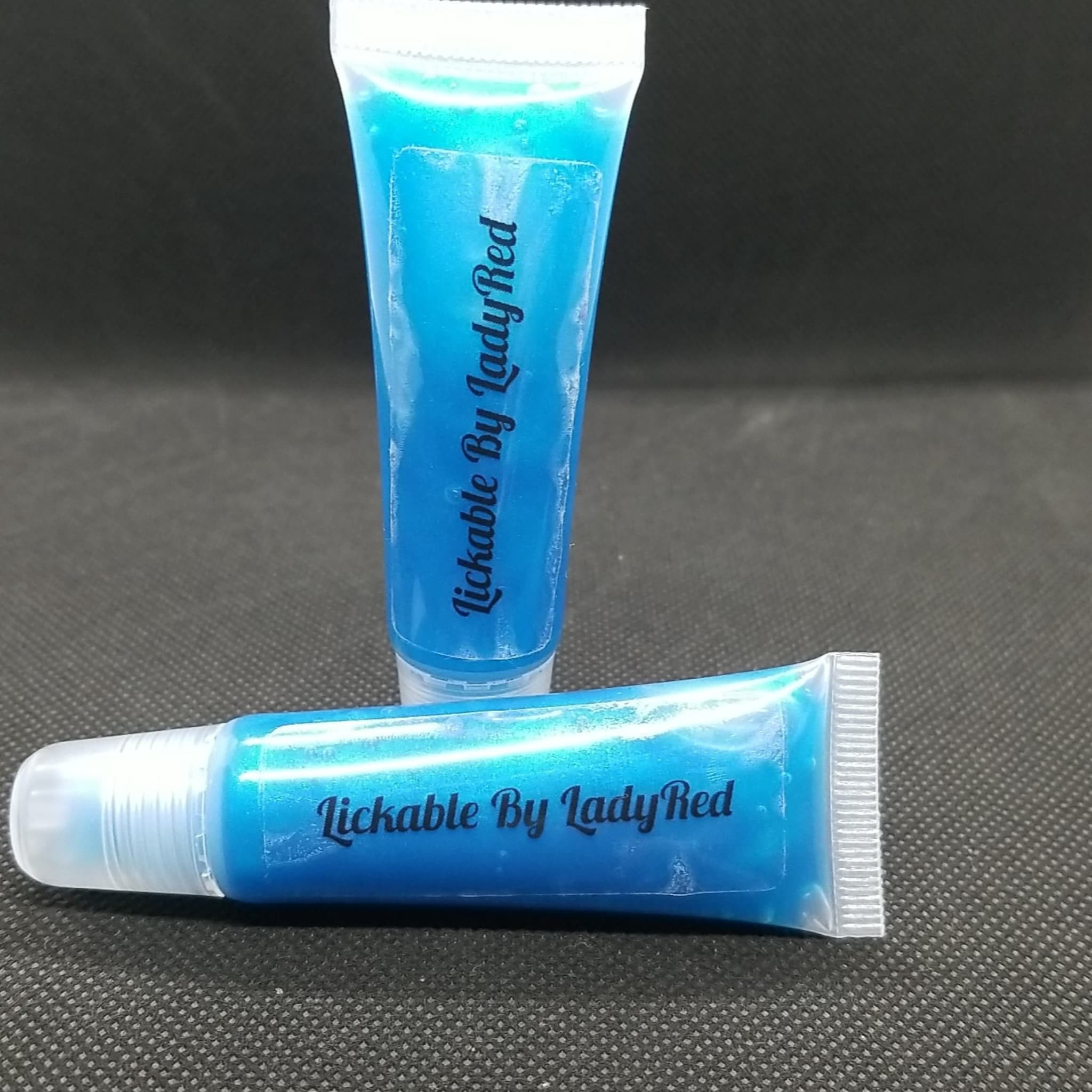 Lip gloss tubes with blue liquid and "Lickable By LadyRed" text on black background.
