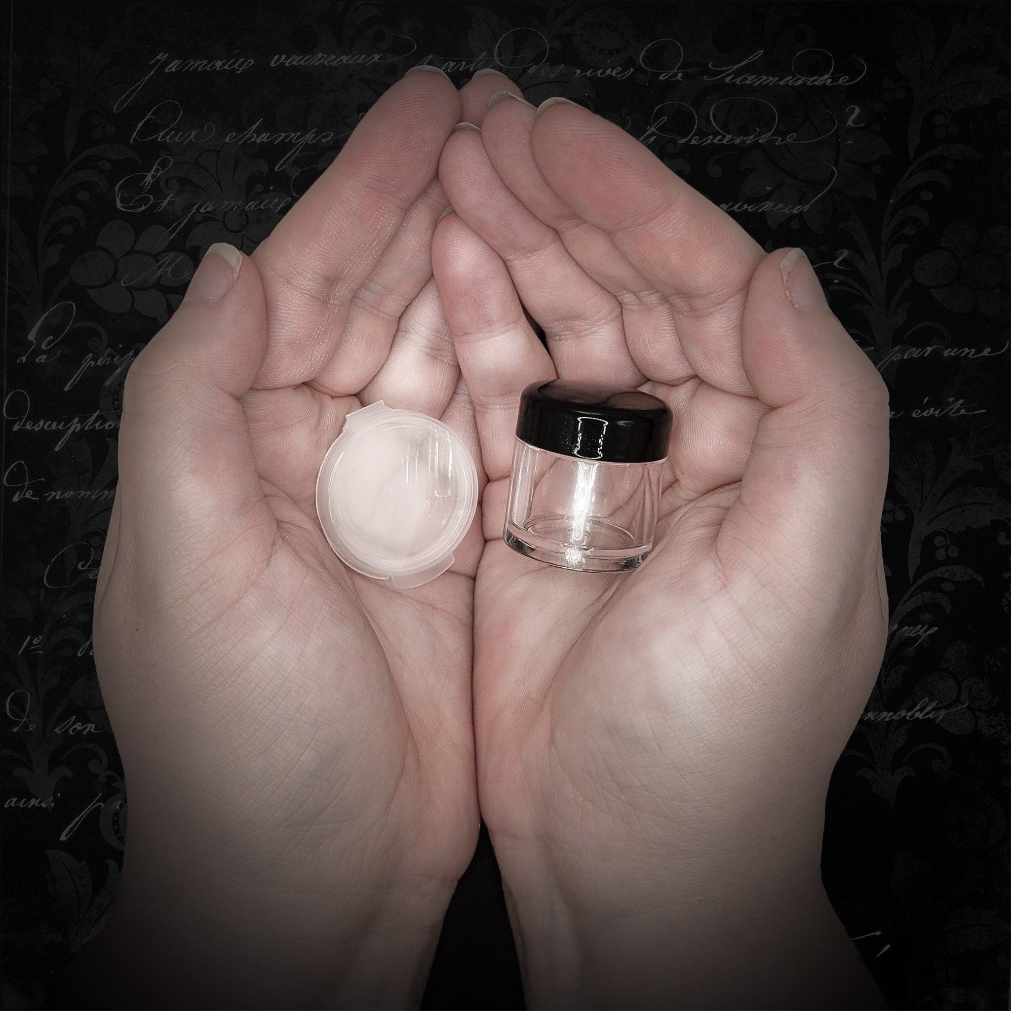 Small clear glass jar with black lid, held in cupped hands against a floral background