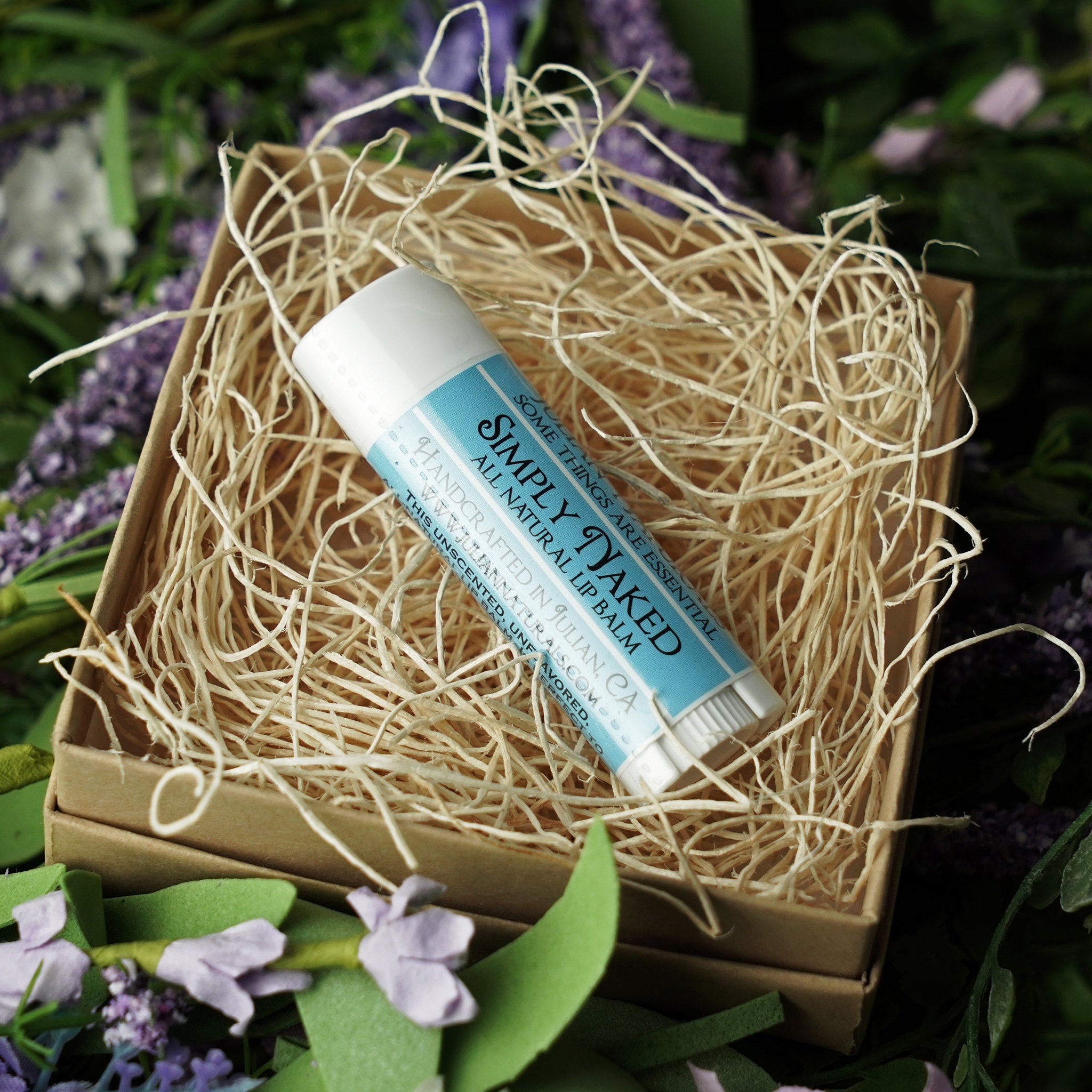 Lip balm tube with blue label, white tube, and Simply Naked text, in a box with straw filler