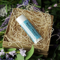 Lip balm tube with blue label, white tube, and Simply Naked text, in a box with straw filler