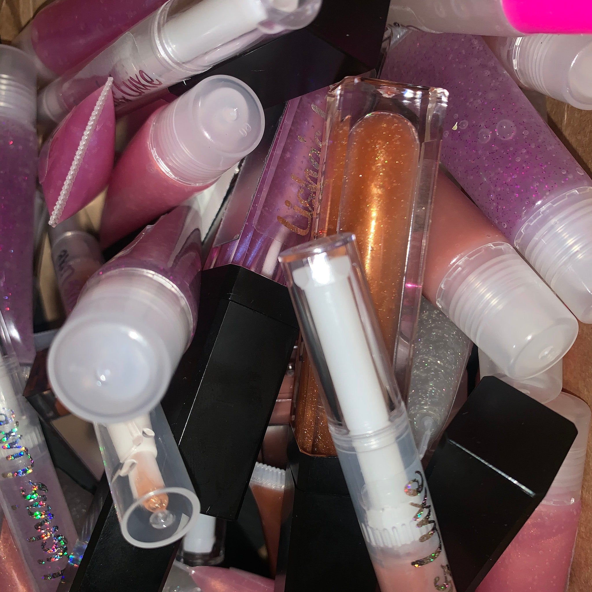 Lip gloss tubes in pink, purple, and clear with LishasLuxe text visible, various colors and textures