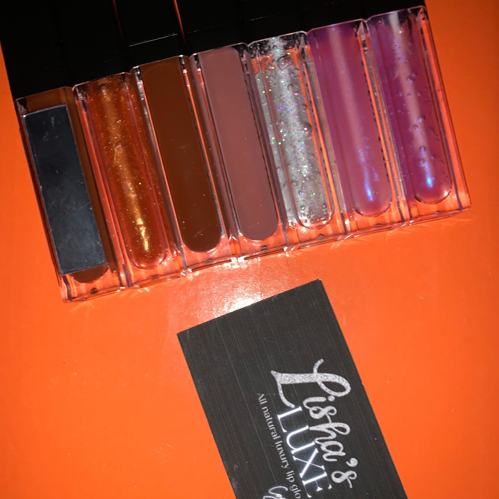 Lip gloss tubes in clear plastic with black caps, various colors and glitter, Lishas Luxe branding