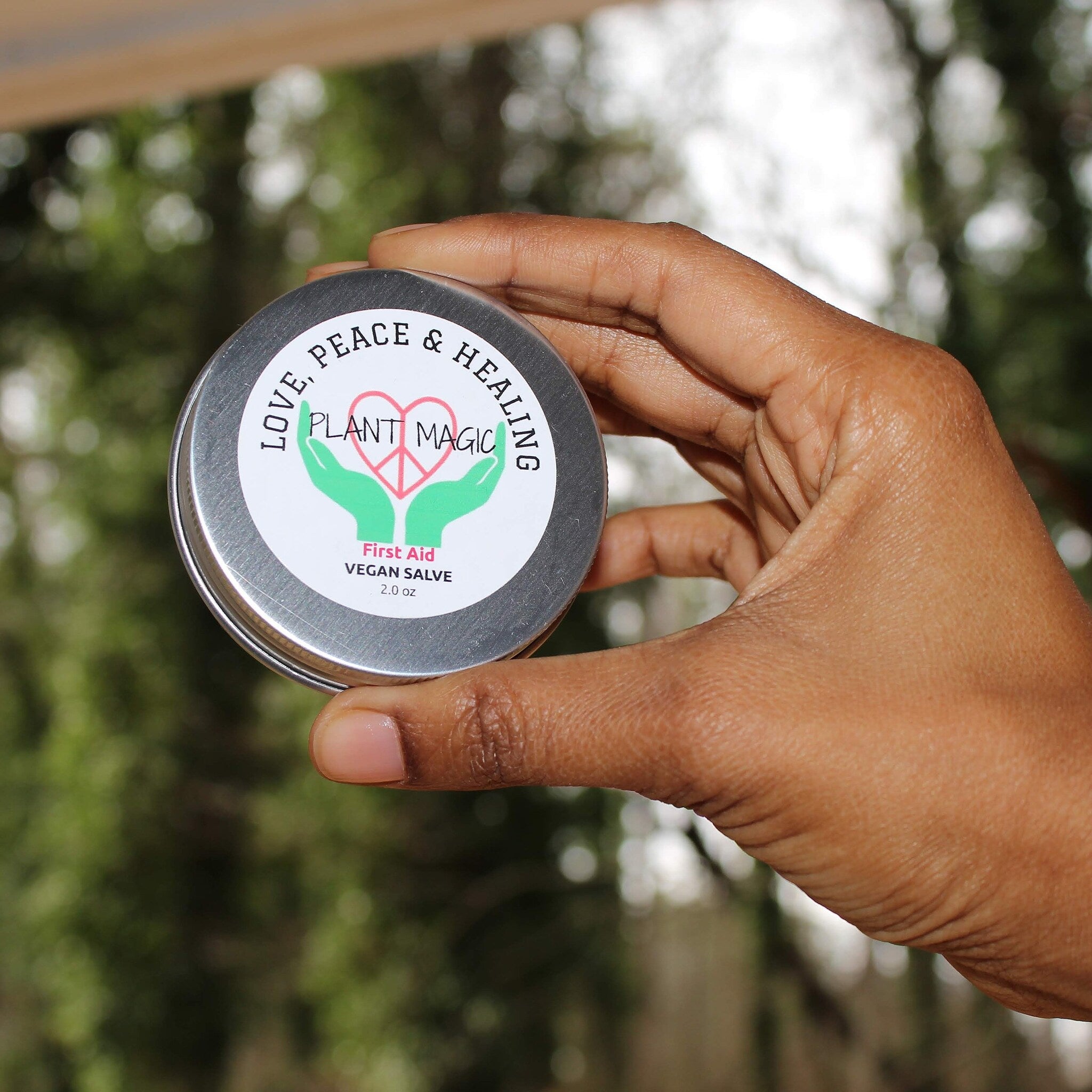 Vegan salve tin held in hand, silver metal, white label with green and pink text, Plant Magic brand