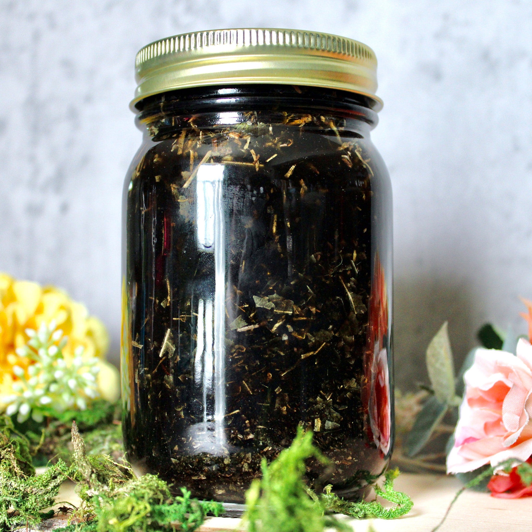 Glass jar with gold lid, dark liquid, and dried herbs inside, on wooden surface
