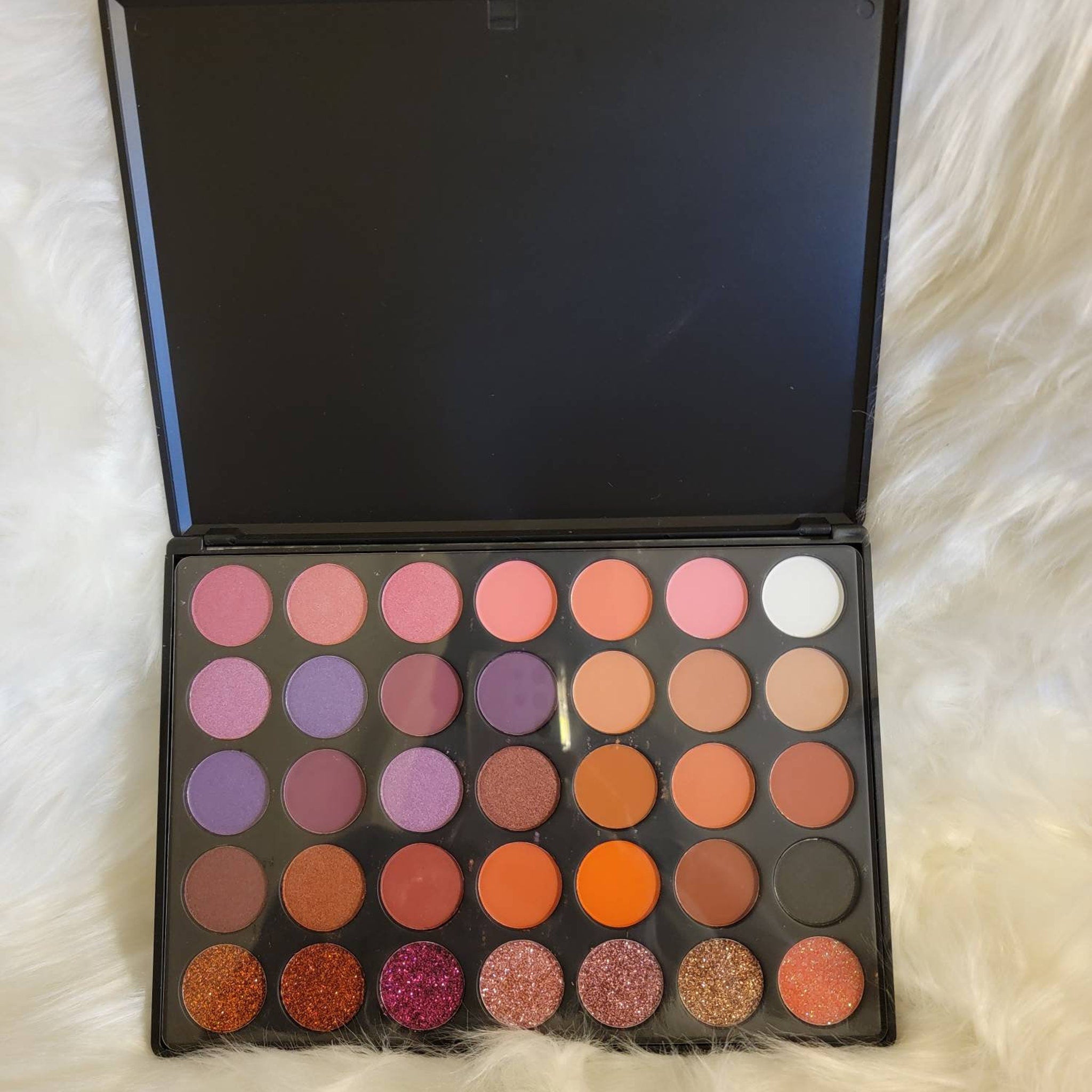 Close-up of shimmering teal and bronze eyeshadow pans in 35-color palette with smooth metallic finish