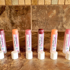 Tinted lip balm tubes with pink and white labels, Bubble Love Boutique brand, on a brown surface.