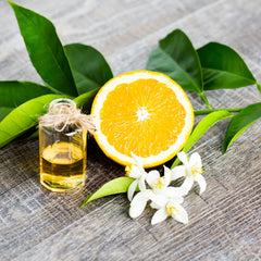 Orange slice with green leaves and a small bottle on a wooden surface
