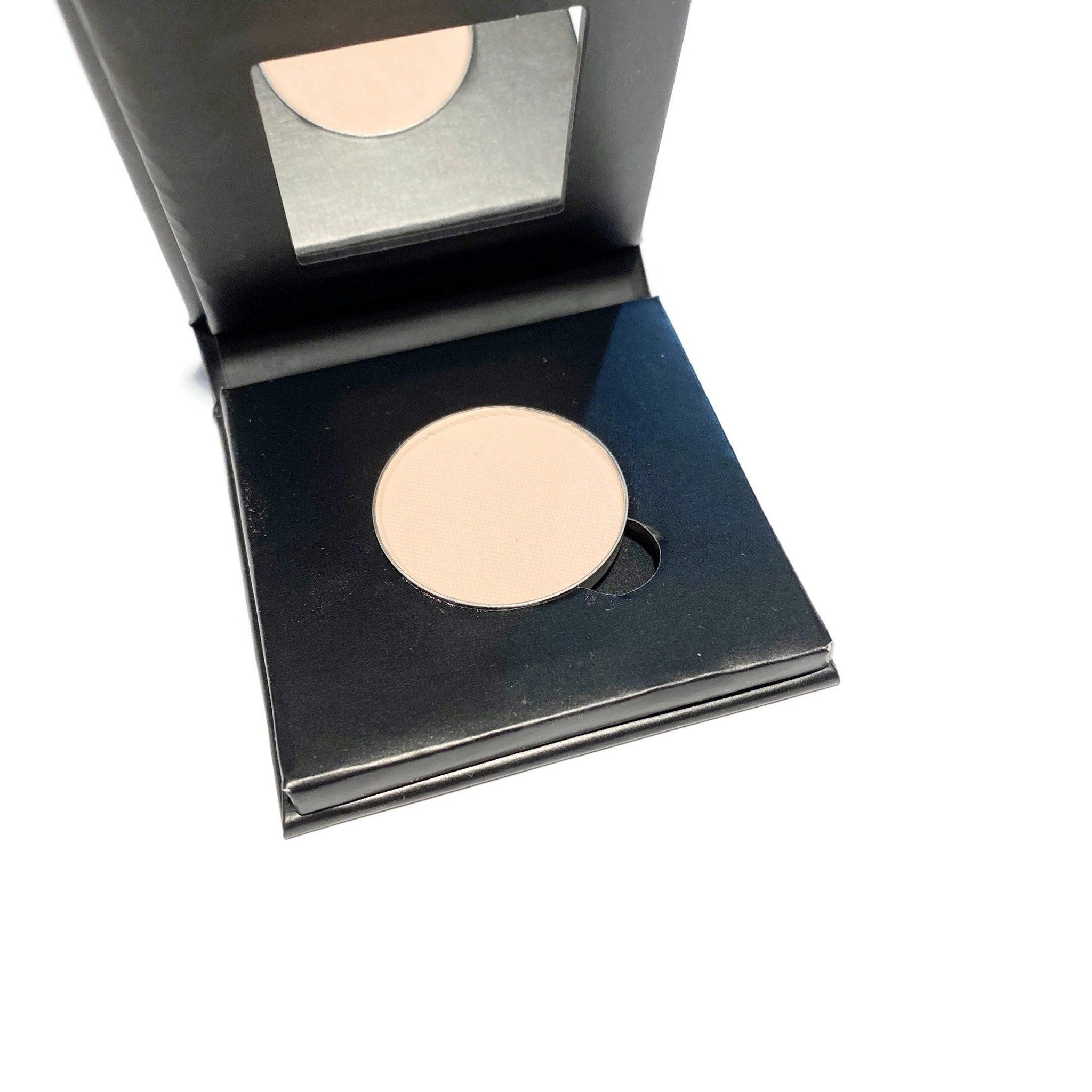 Close-up of barely bisque eyeshadow pan in refillable paperboard compact showing matte texture
