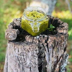 Skin care scrub in a clear glass jar with green contents, on a weathered wood stump