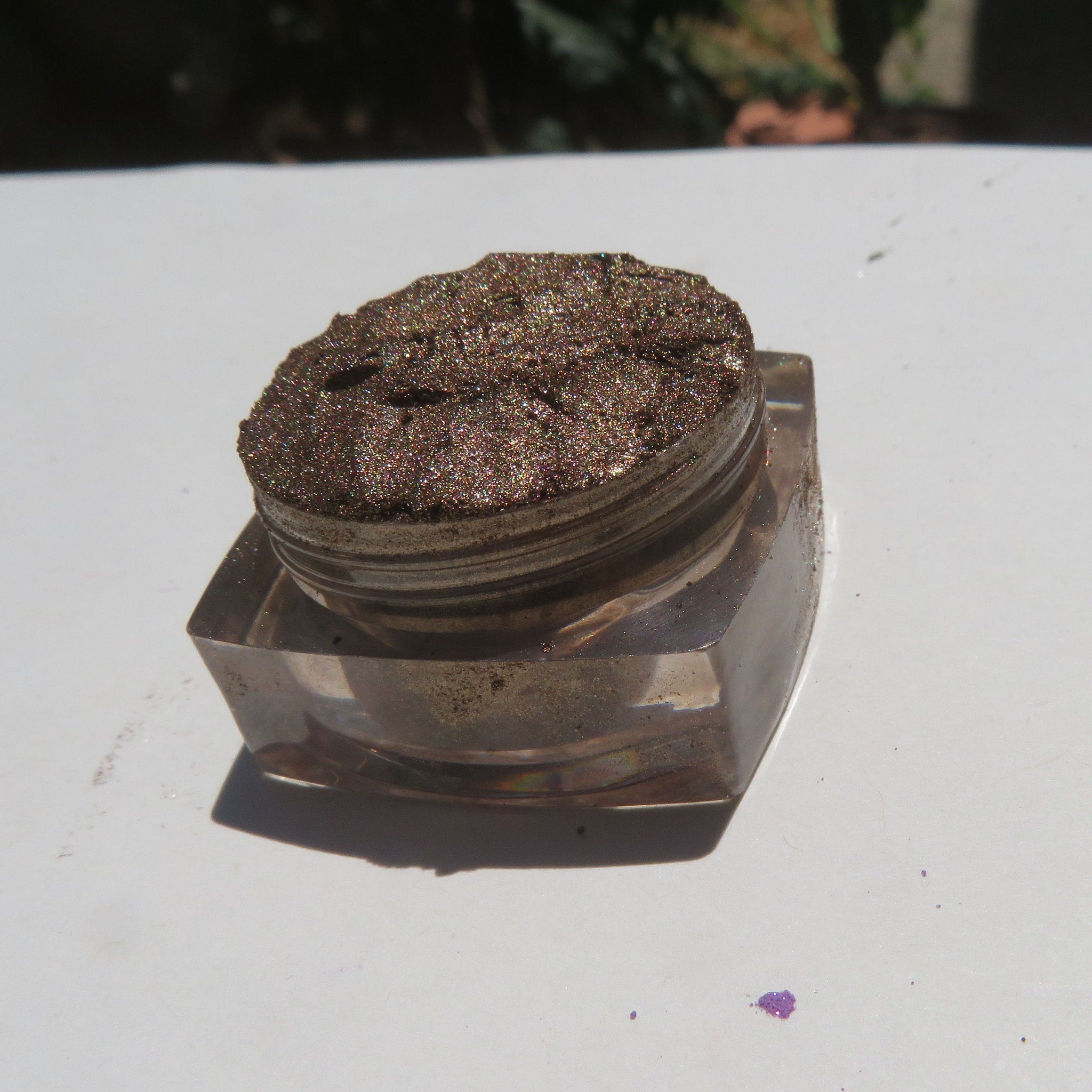 Close-up of loose chocolate brown eyeshadow with gold shimmer particles scattered across textured surface