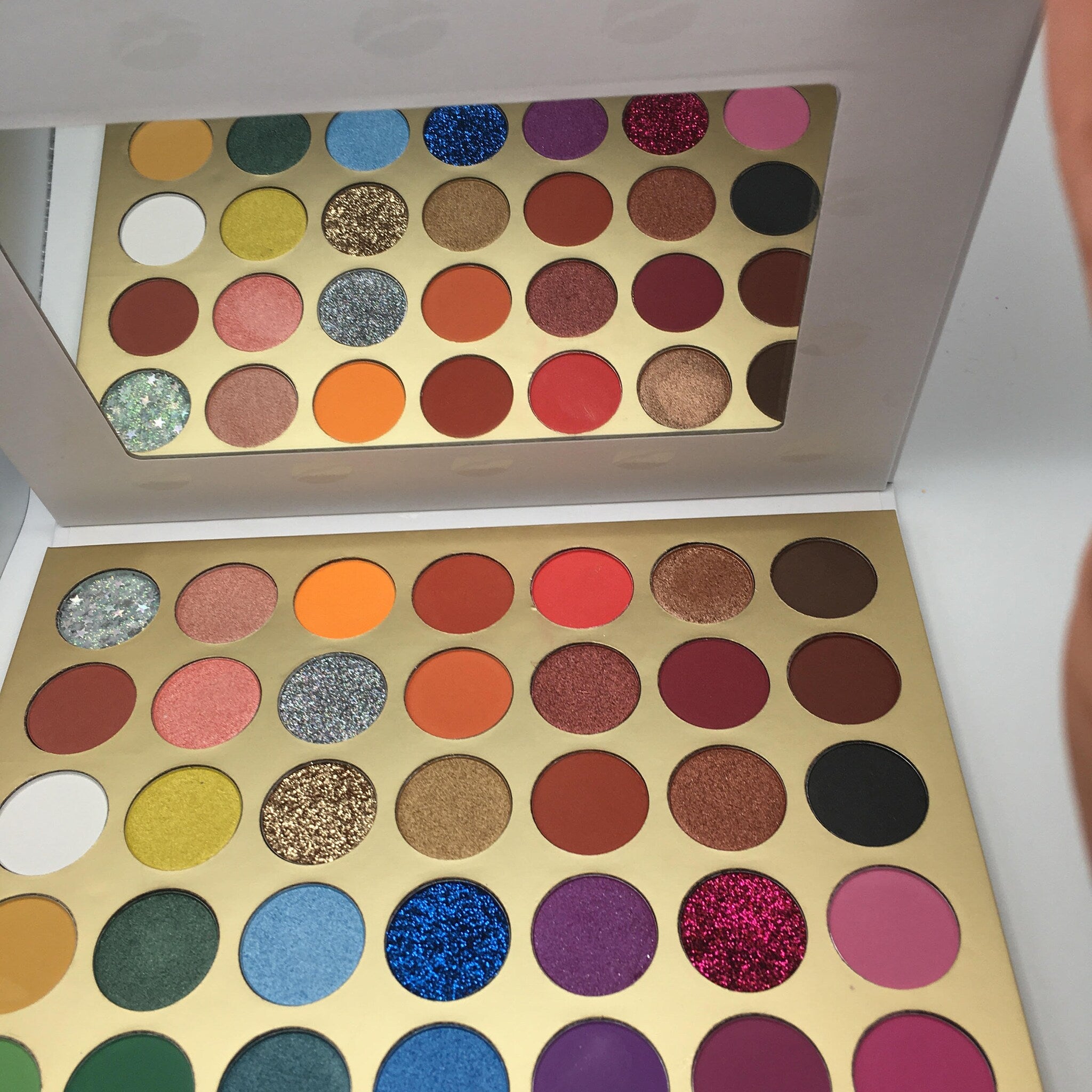 Open 35-color eyeshadow palette with mirror, displaying matte and shimmer shades in warm neutrals and bold hues.