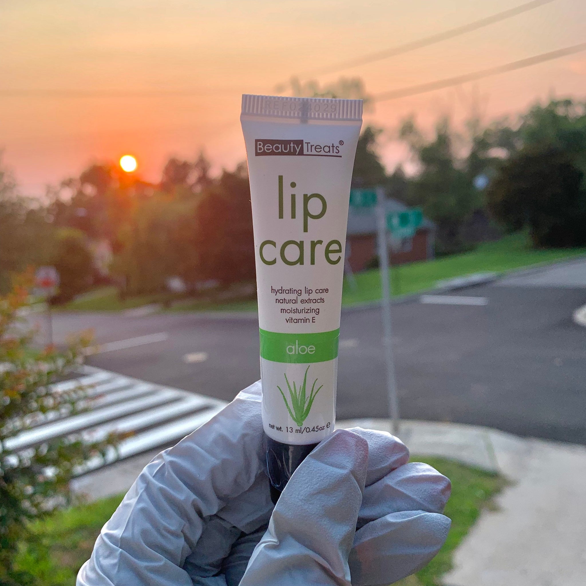 Lip care tube with white, green and black text, held in a gloved hand, Beauty Treats brand