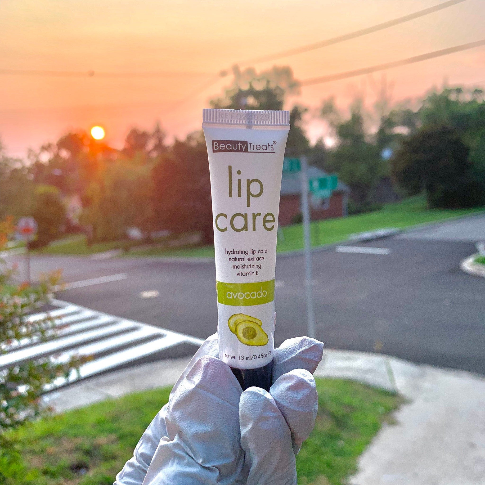Lip care tube with white and green label, held in gloved hand, Beauty Treats brand
