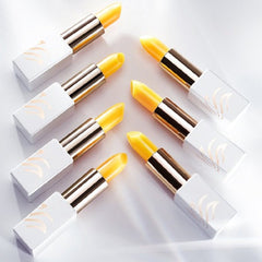 Lipsticks with yellow balm, white and gold casing, and gold logo detail, arranged on white surface