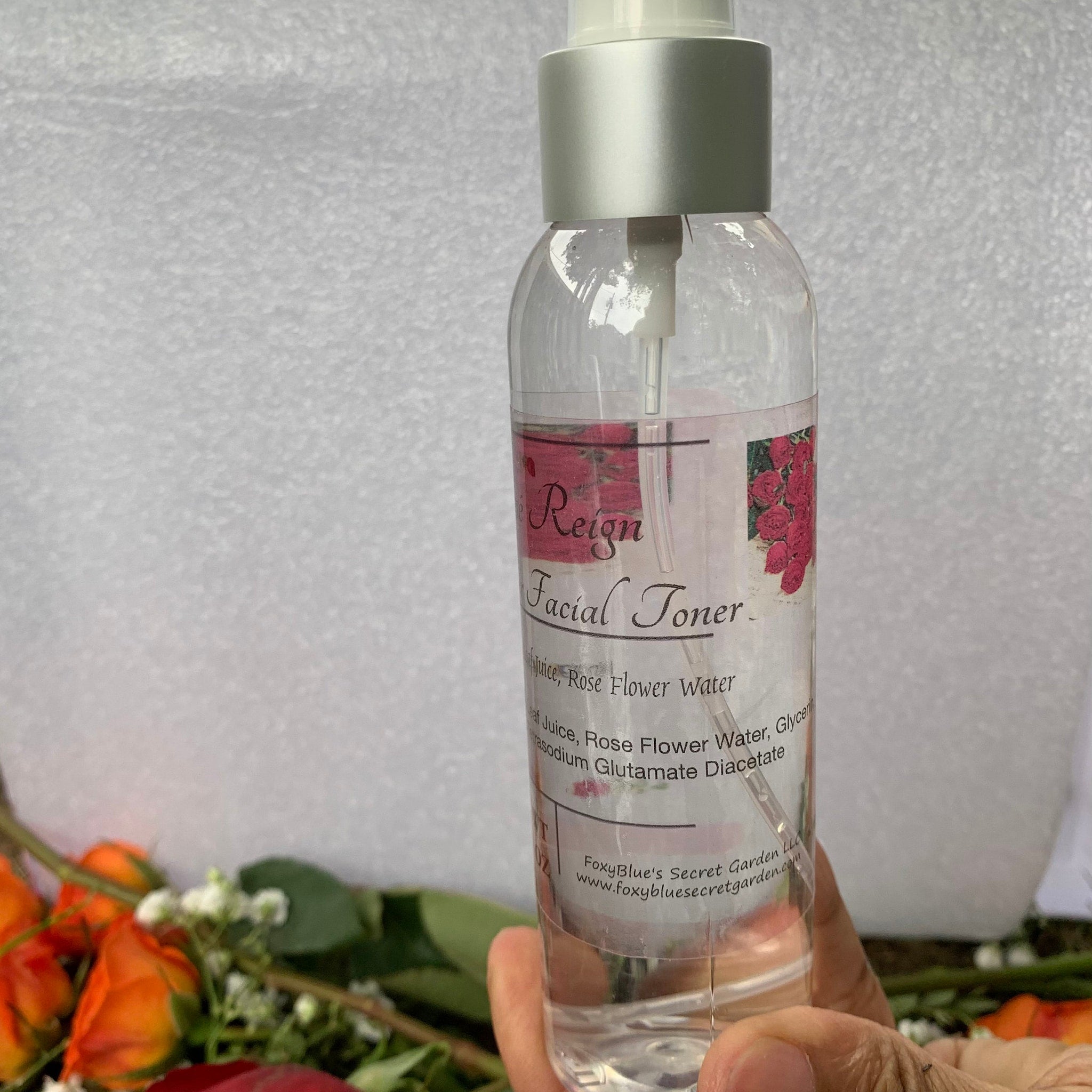 Facial toner bottle with silver cap, clear liquid, and "Reign" label with rose design held by hand