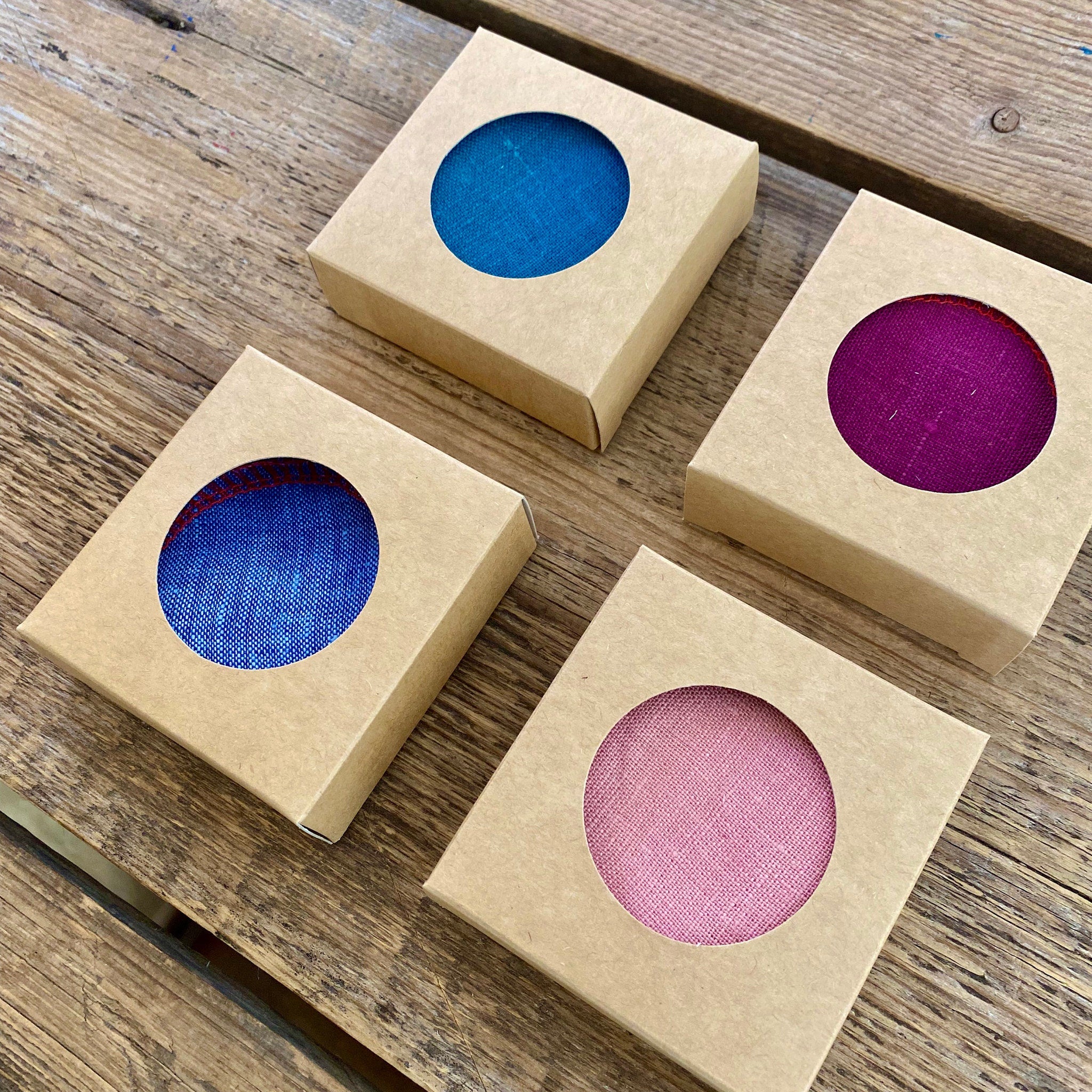 Round fabric swatches in blue, pink, and purple colors, visible through cardboard packaging on wood surface