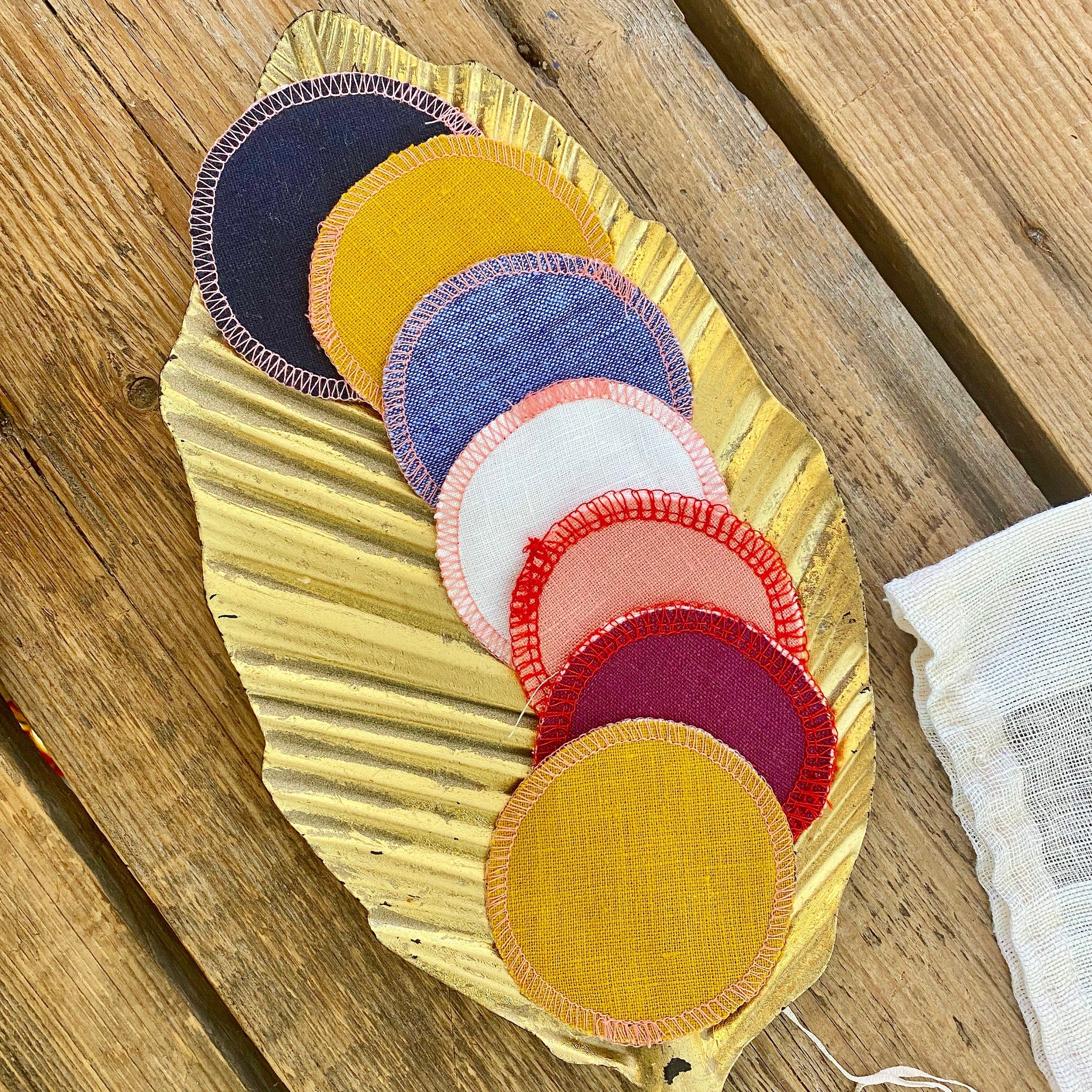 Reusable face rounds in various colors, stitched edges, arranged on a gold leaf, with a white cloth.