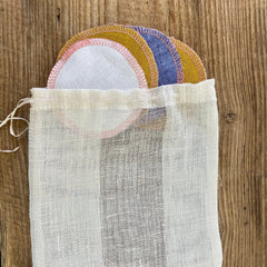Reusable facial rounds in various colors, white linen bag with drawstring, wooden background