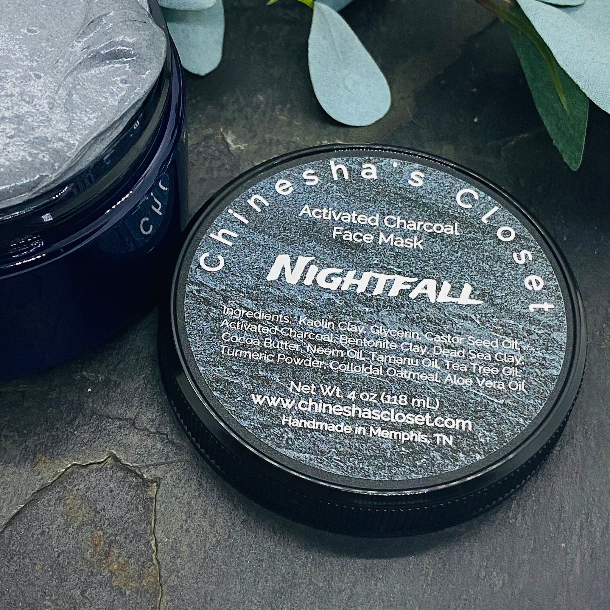 Activated charcoal face mask in dark blue jar, gray mask inside, and brand name on lid