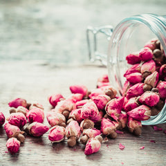 Dried rose buds, pink and brown buds, scattered on wooden surface with glass jar